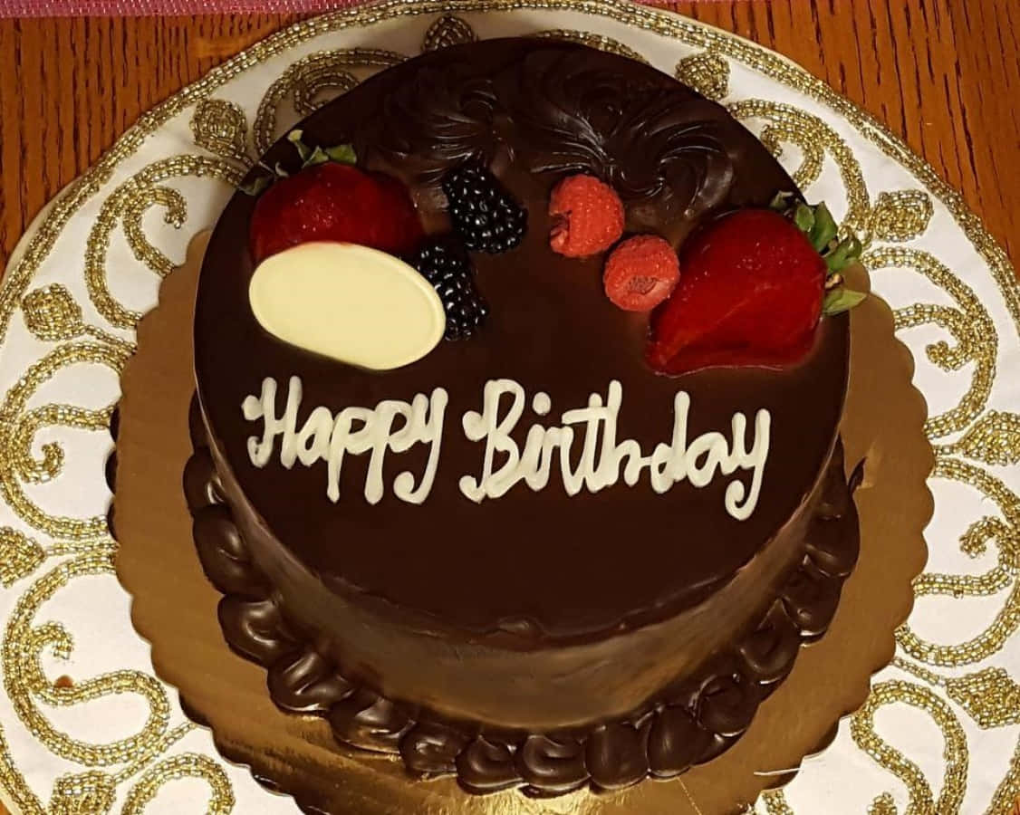 生日蛋糕 桌布 壁紙 — 一個豐富的朱古力生日蛋糕，飾以新鮮漿果和白色糖霜字句，優雅地放在金邊碟子上。