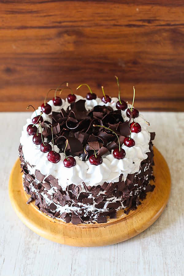 Black Forest Cake 桌布 壁紙 — 一個豐富的黑森林蛋糕，上面放有鮮奶油、朱古力碎和鮮紅櫻桃，置於木板上。