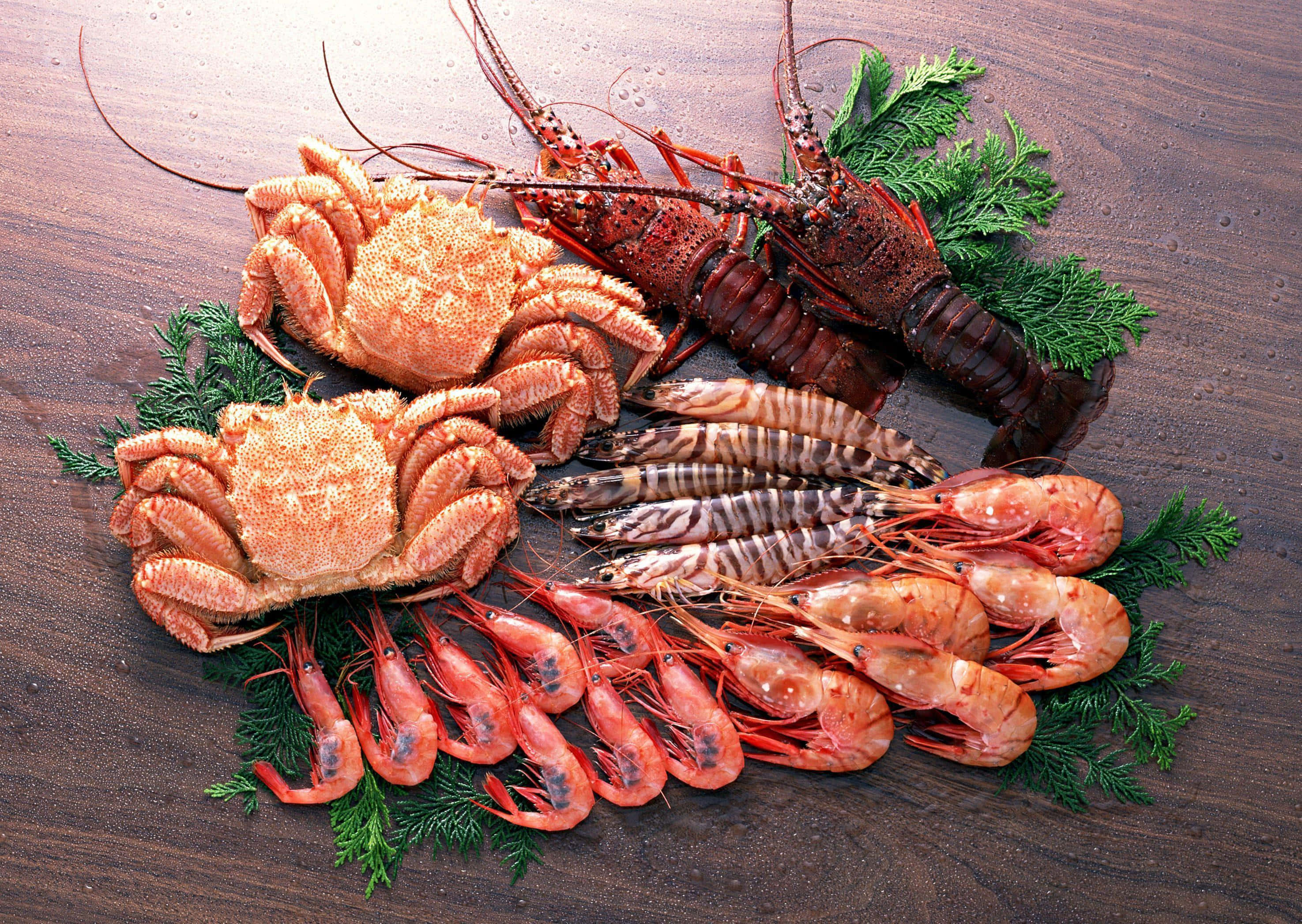 Seafood 桌布 壁紙 — 一個豐盛的海鮮拼盤，包含蟹、龍蝦、蝦和對蝦，藝術性地擺放在深色木質表面上，搭配新鮮蔬菜。