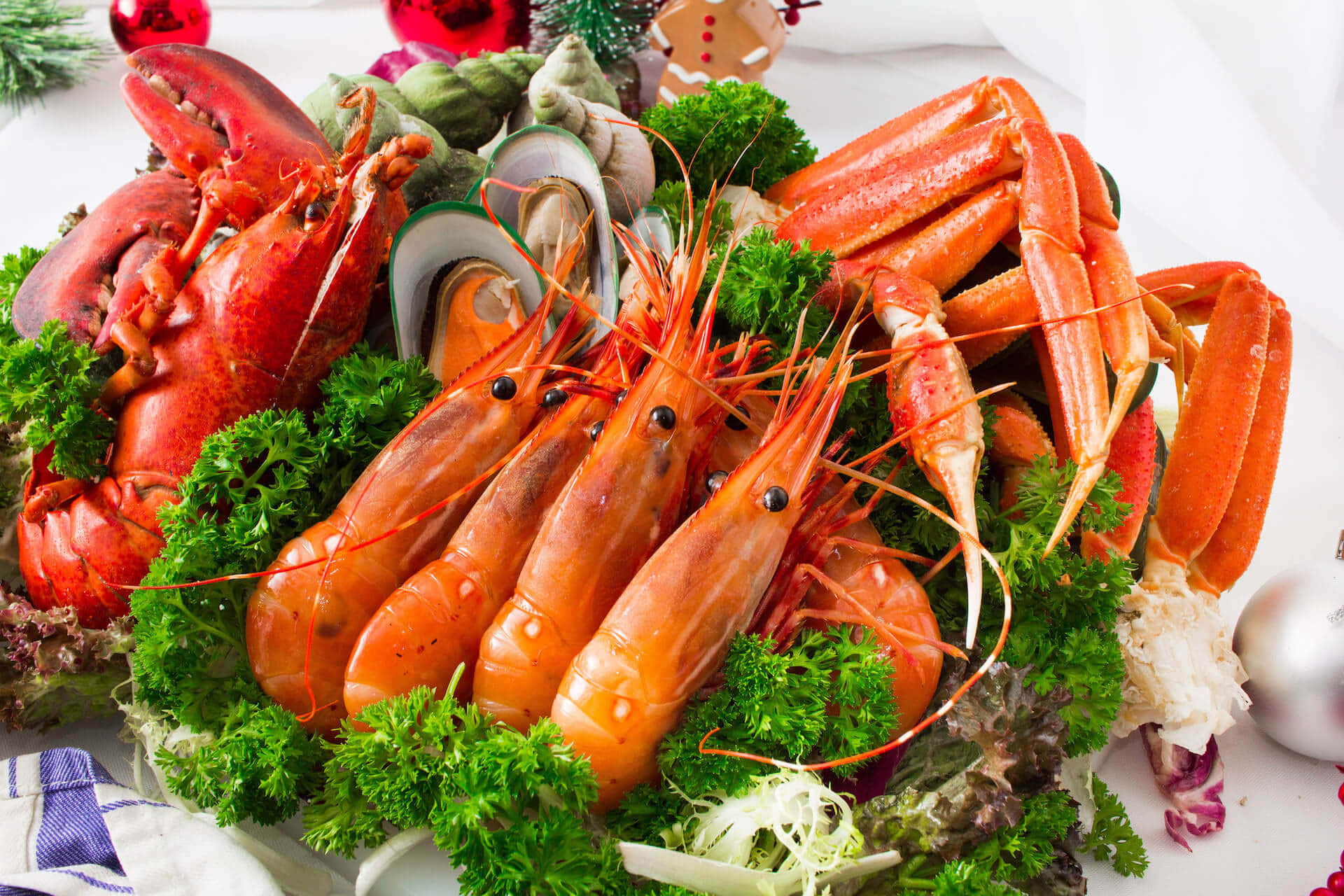 Seafood 桌布 壁紙 — 一個豐盛的海鮮拼盤，有鮮紅色的龍蝦、蟹腳和蝦，放在新鮮的綠色歐芹上，置於白色桌布上。