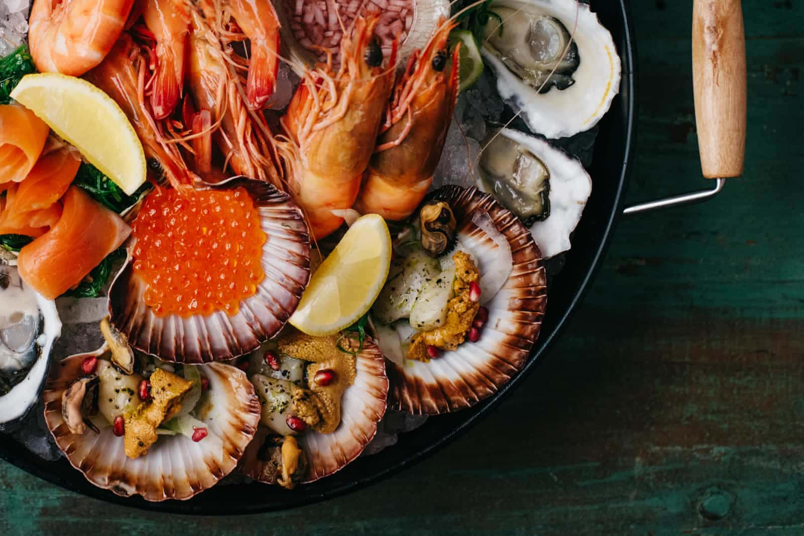 Seafood 桌布 壁紙 — 一個豪華海鮮拼盤，包括蝦、生蠔、扇貝、三文魚籽和檸檬角，放在冰上，盛載於黑色碗中。