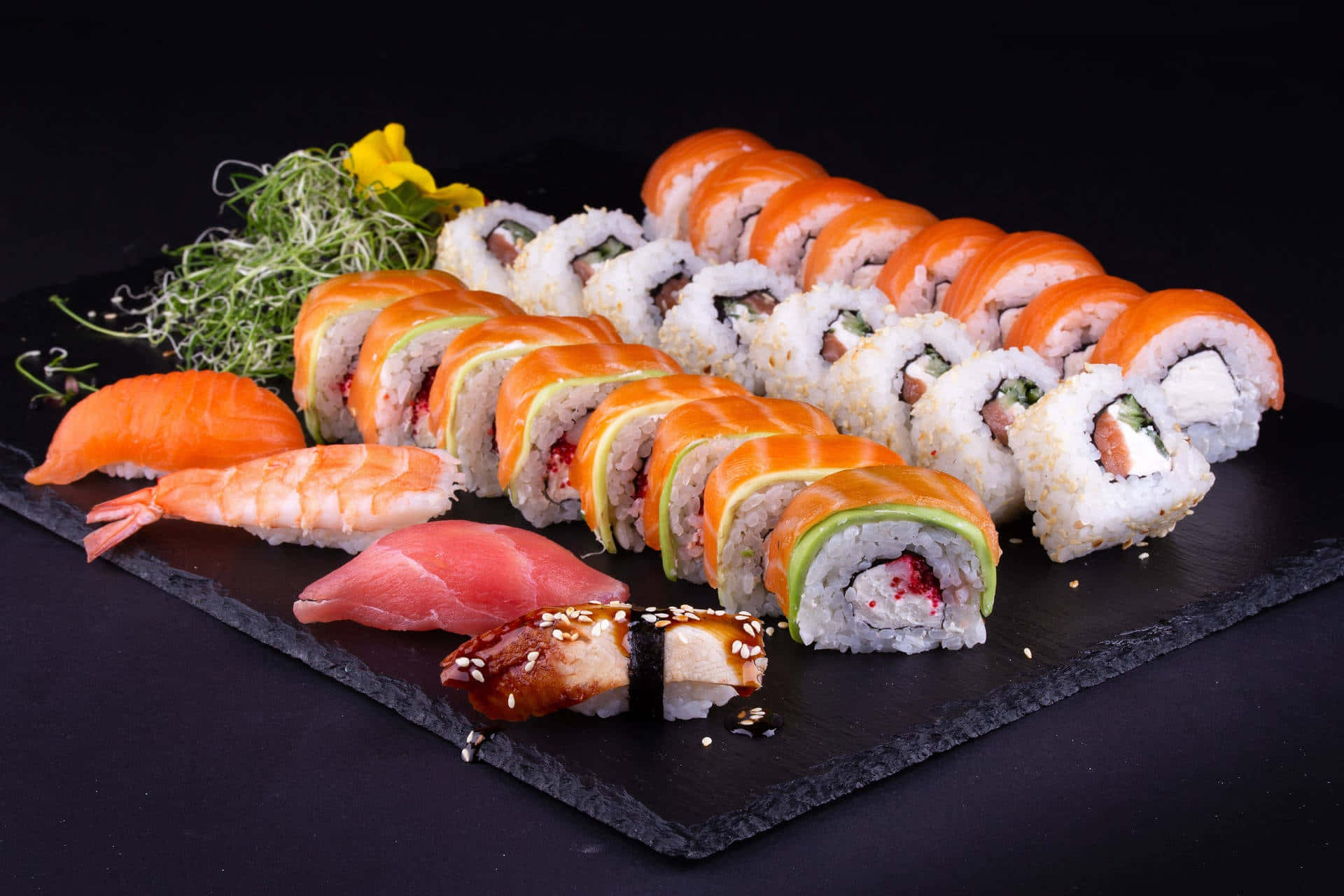 Sushi 桌布 壁紙 — 一個豪華的壽司拼盤，包括三文魚卷、吞拿魚握壽司、蝦天婦羅和配菜，放在黑色石板上的深色背景中。
