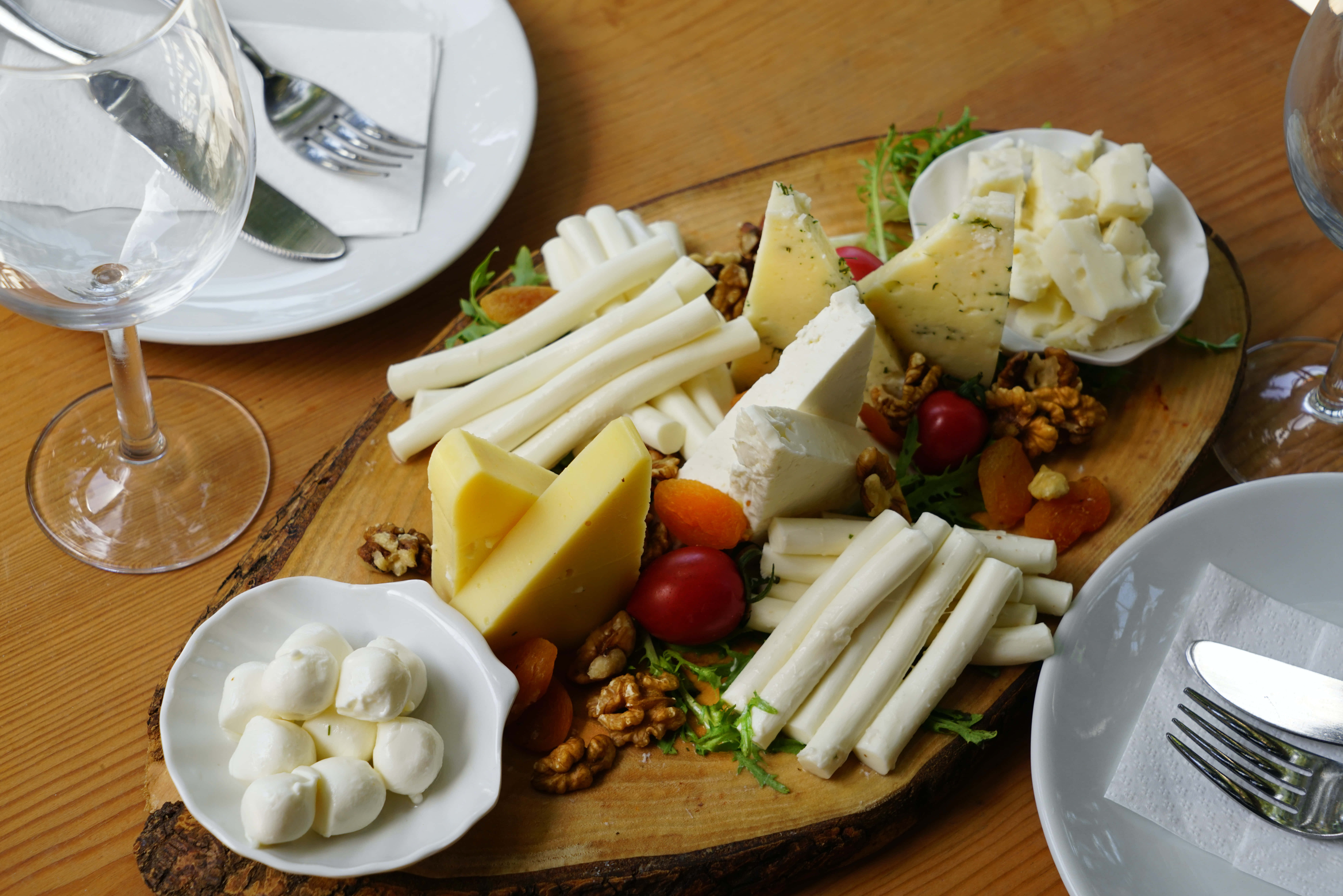 Cheese 桌布 壁紙 — 一個質樸的木板上放滿了各式各樣的芝士、堅果和車厘茄，放在溫暖的木桌上，旁邊有酒杯。