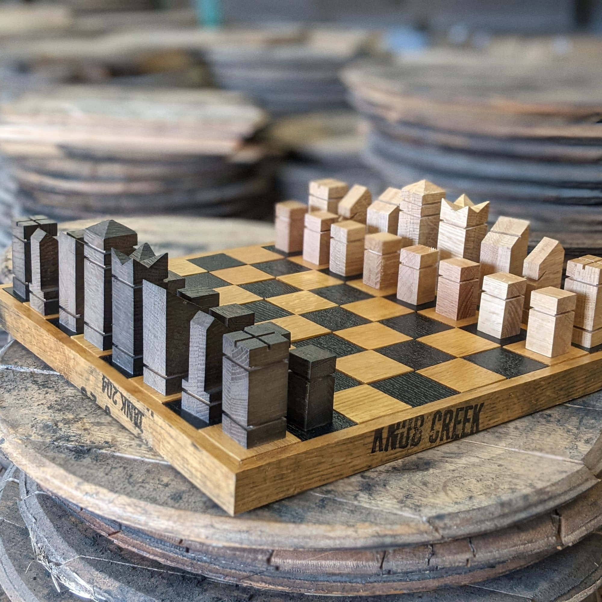 Chessboard 桌布 壁紙 — 一個質樸的木製國際象棋套裝，帶有城市景觀主題的棋子，放置在工作室環境中堆疊的木桶上。