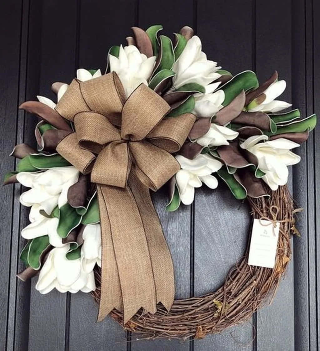 Spring Wreaths 桌布 壁紙 — 一個質樸的葡萄藤花環，點綴著白色木蘭花、綠葉和一個大型麻布蝴蝶結，掛在深色木門上。