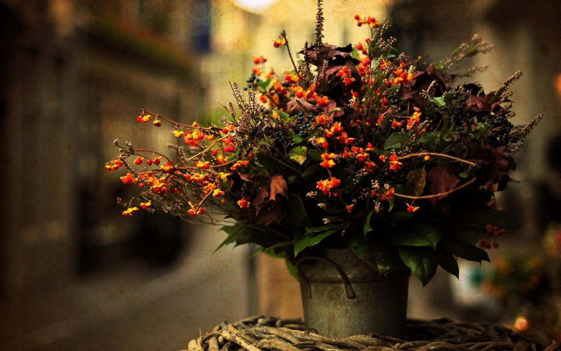 Floral Arrangement 桌布 壁紙 — 一個質樸的金屬桶裝滿了秋天的漿果和樹葉，放在編織墊上，背景是柔和模糊的街道。