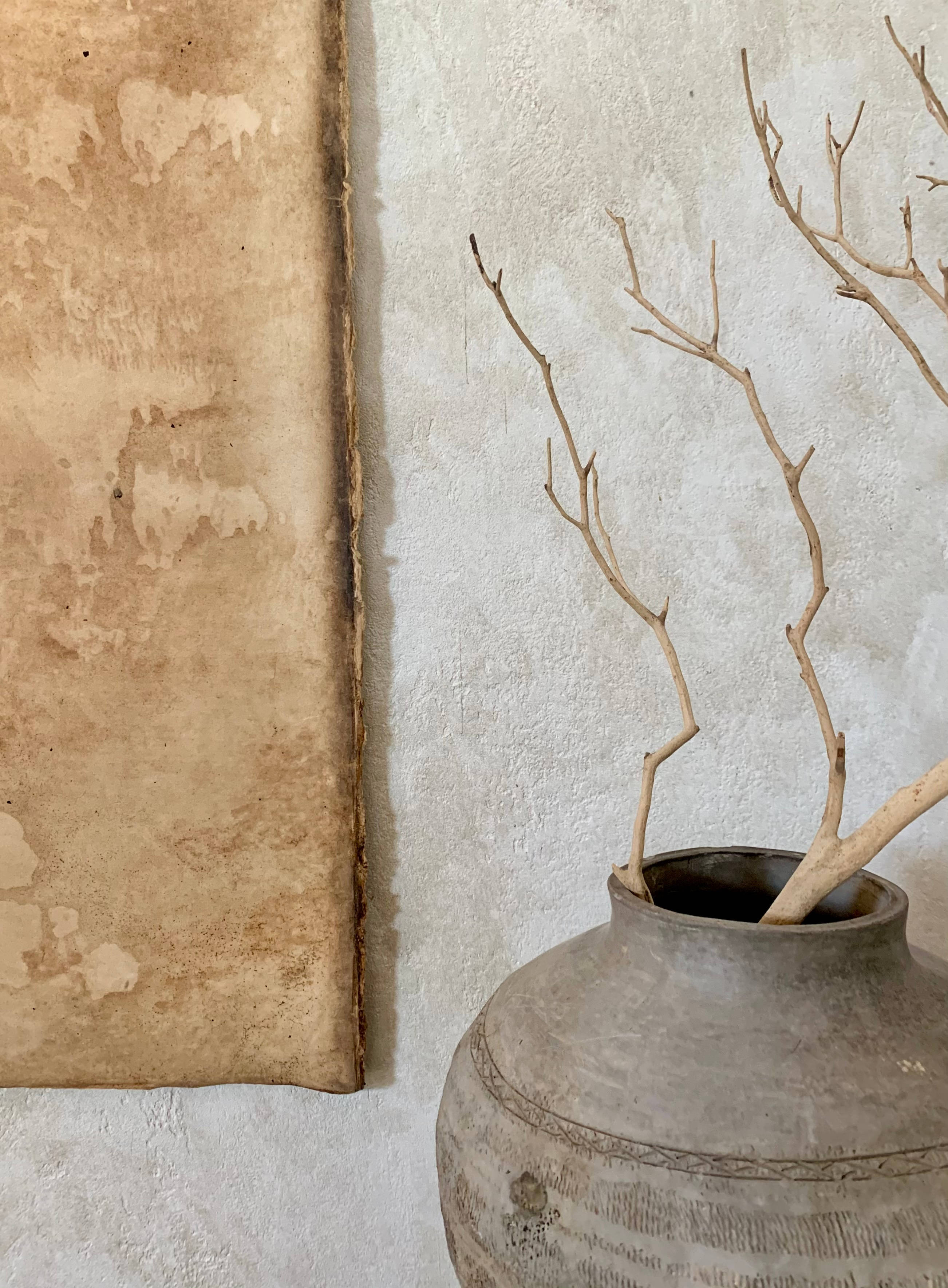 Beige Minimalist 桌布 壁紙 — 一個質樸的陶罐插著光禿禿的樹枝，旁邊放著一張陳舊的羊皮紙，背景是帶紋理的白色牆壁。