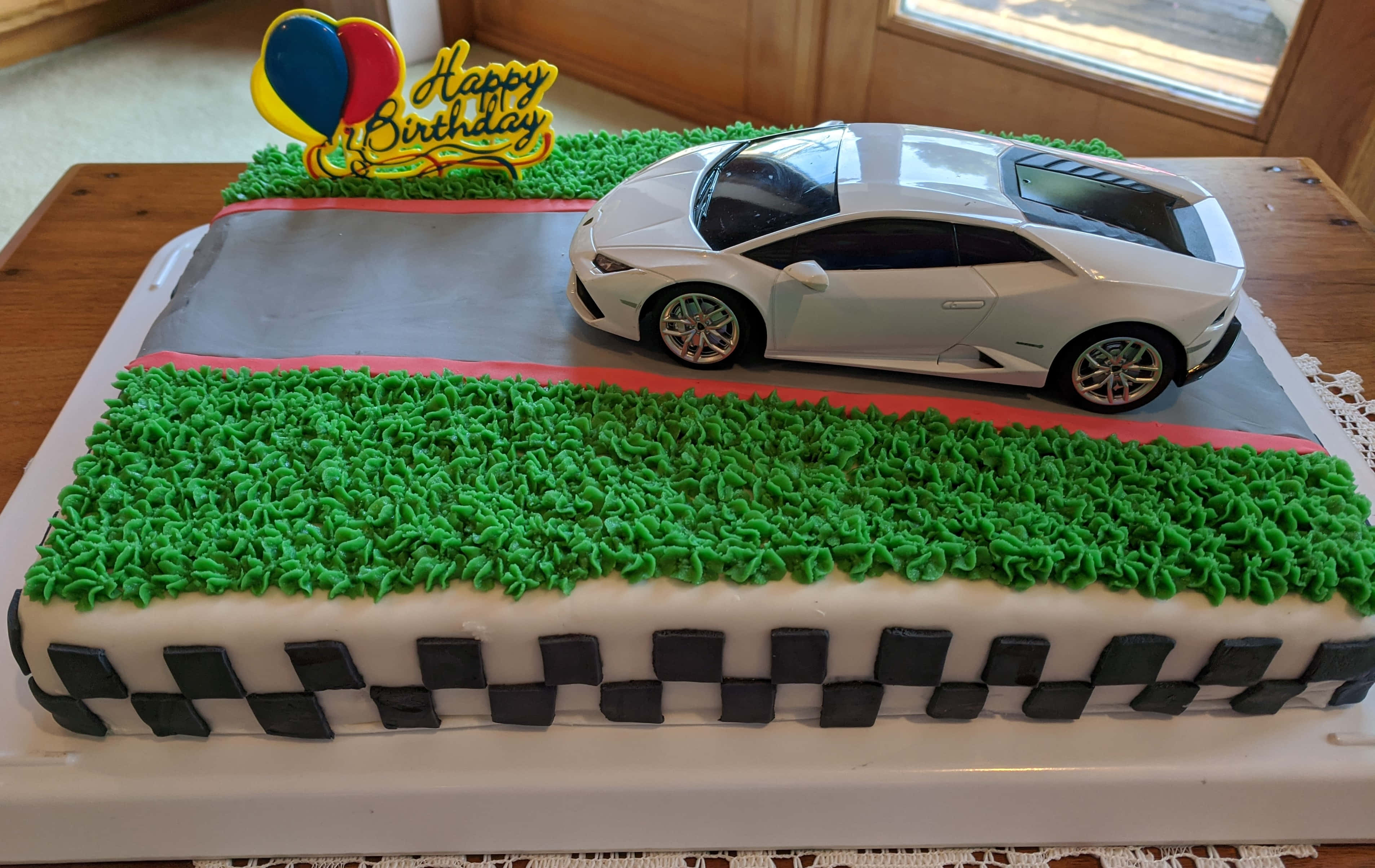 Cake Fondant 桌布 壁紙 — 一個賽車場形狀的生日蛋糕，白色跑車放在綠色糖霜草地上，並有棋盤邊框。