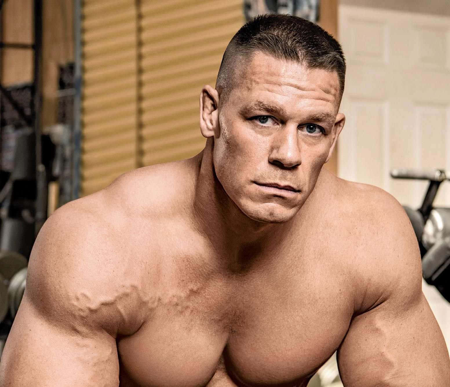John Cena 桌布 壁紙 — 一個赤裸上身的肌肉男，擁有強烈的藍色眼睛，在健身房環境中直視鏡頭。