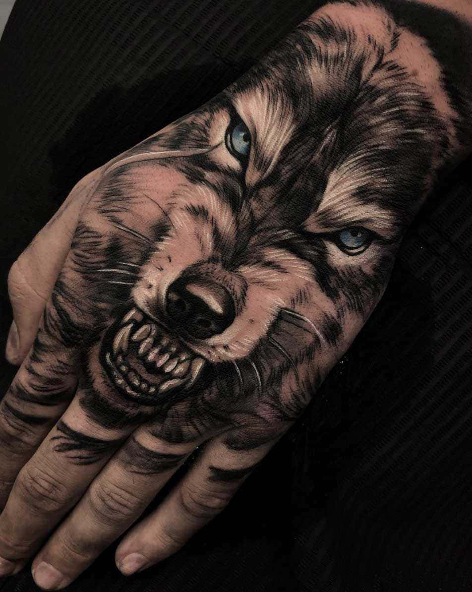 Wolf Tattoo 桌布 壁紙 — 一個超寫實的狼紋身覆蓋了一隻手，有著銳利的藍色眼睛和露出的牙齒，背景為深色。