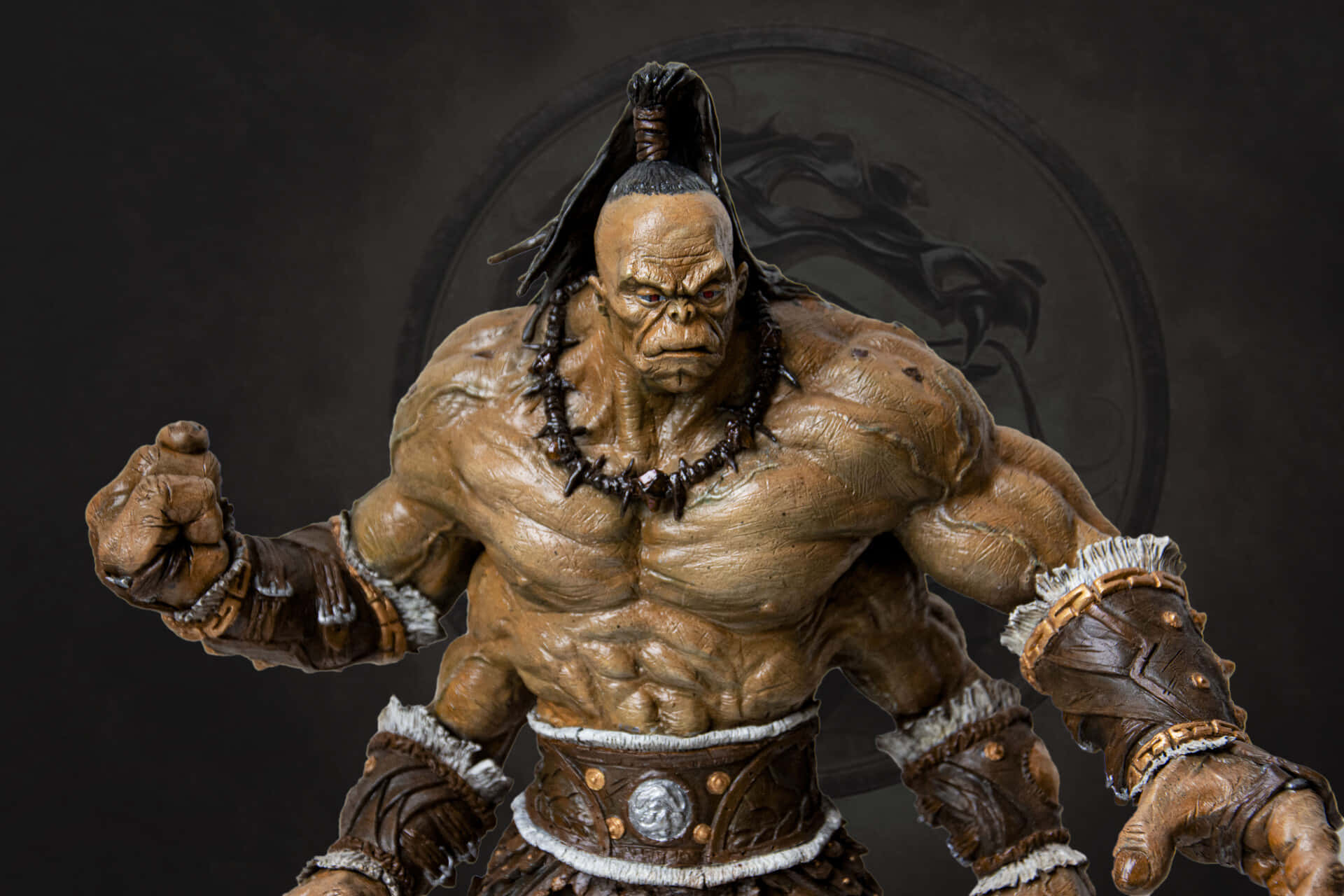 Mortal Kombat Goro 桌布 壁紙 — 一個超詳細的3D渲染肌肉發達的獸人戰士，穿著部落盔甲，表情兇猛，在黑暗圓形徽章背景下擺出侵略性姿勢。