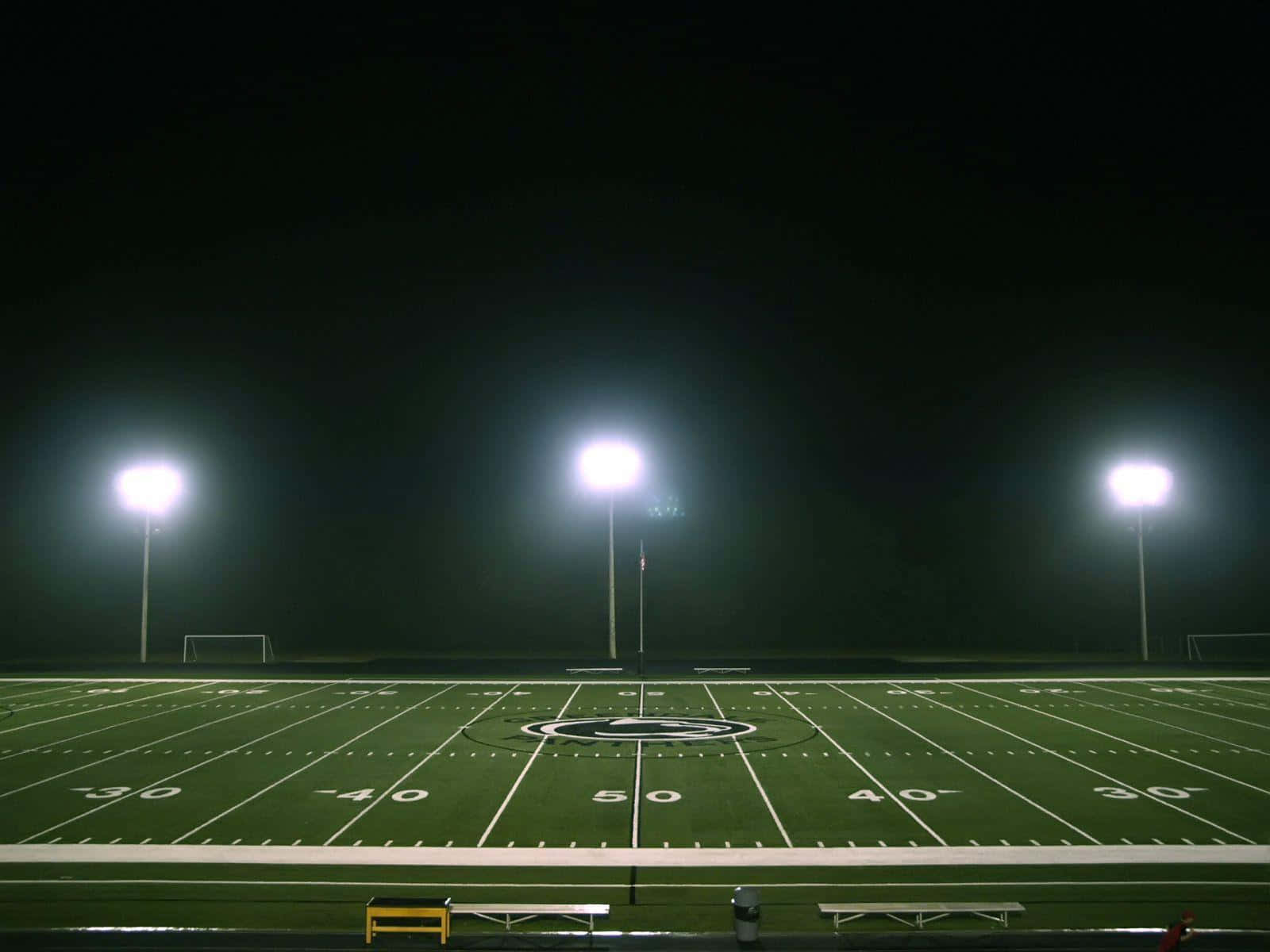 Football Stadium 桌布 壁紙 — 一個足球場被三盞明亮的體育場燈光照亮，背景是漆黑的夜空。