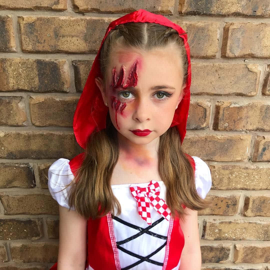 Halloween Face Paint 桌布 壁紙 — 一個身穿沾血小紅帽服裝的年輕女孩，莊嚴地站在風化的磚牆前。