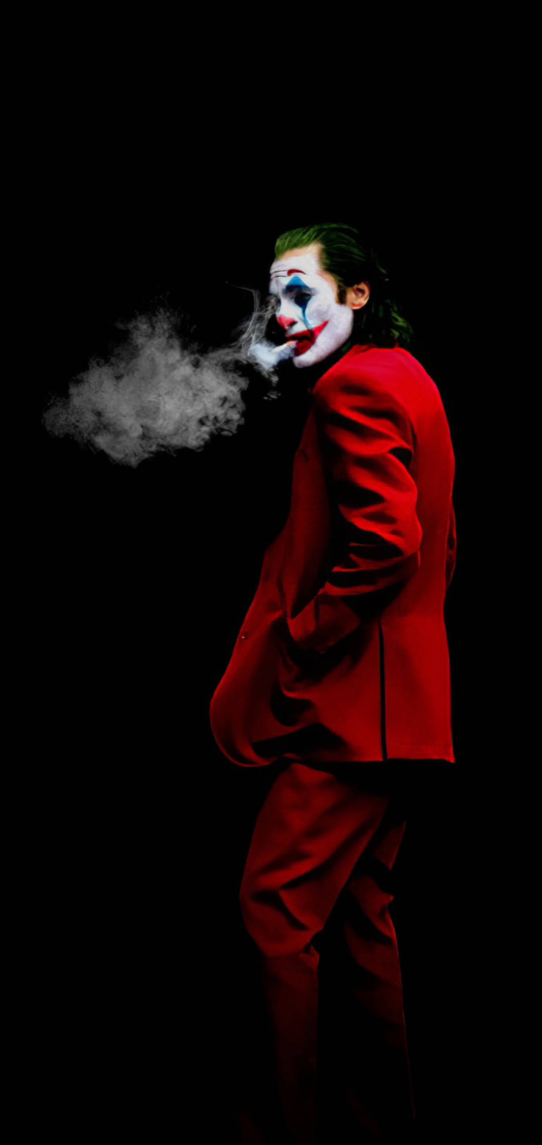 小丑 桌布 壁紙 — 一個身穿紅色西裝、化著小丑妝的可怕人物在黑色背景前吐煙。