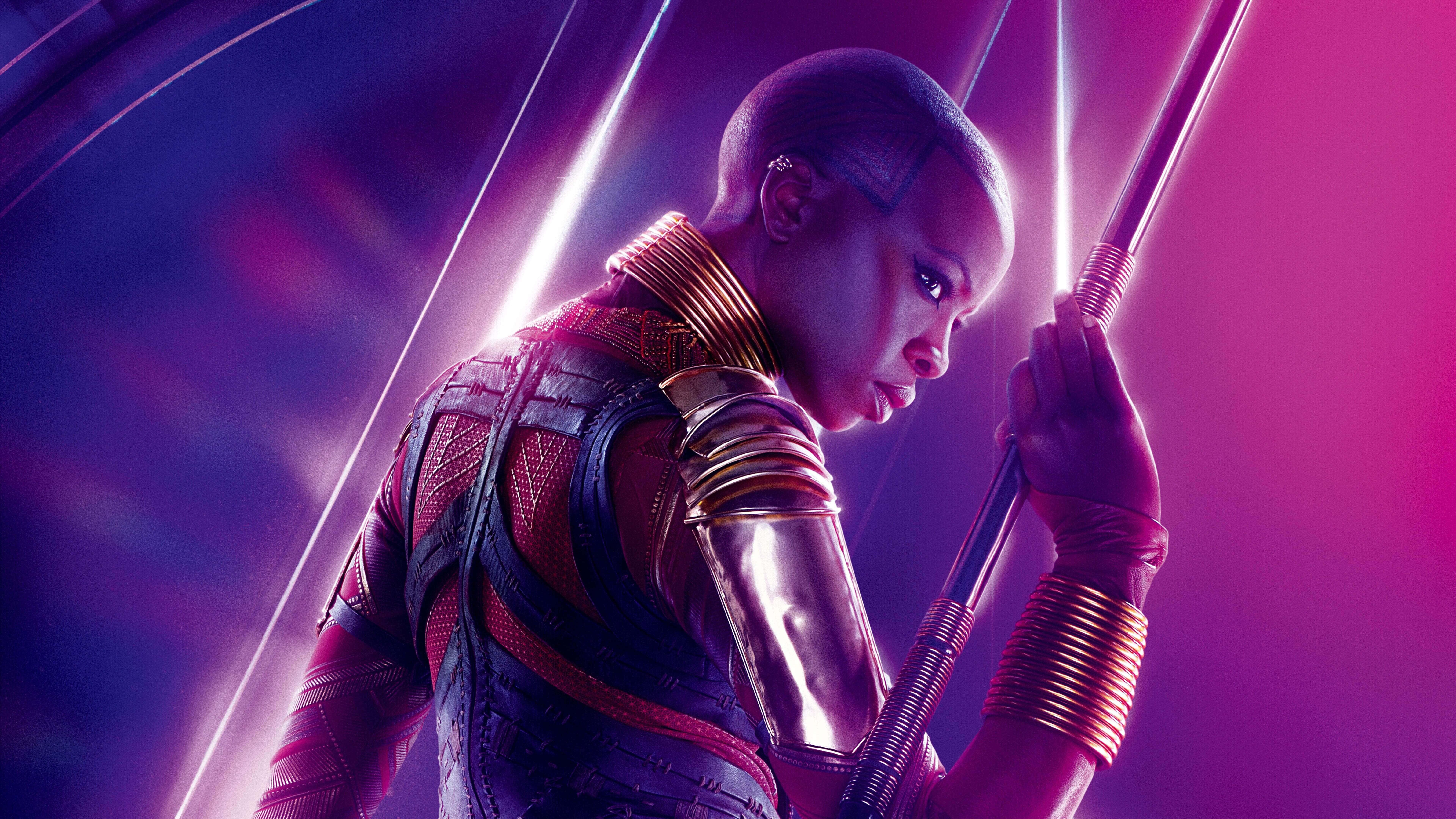 Okoye 桌布 壁紙 — 一個身穿紅金鎧甲的兇猛戰士，在發光的紫藍色宇宙背景下緊握長矛。