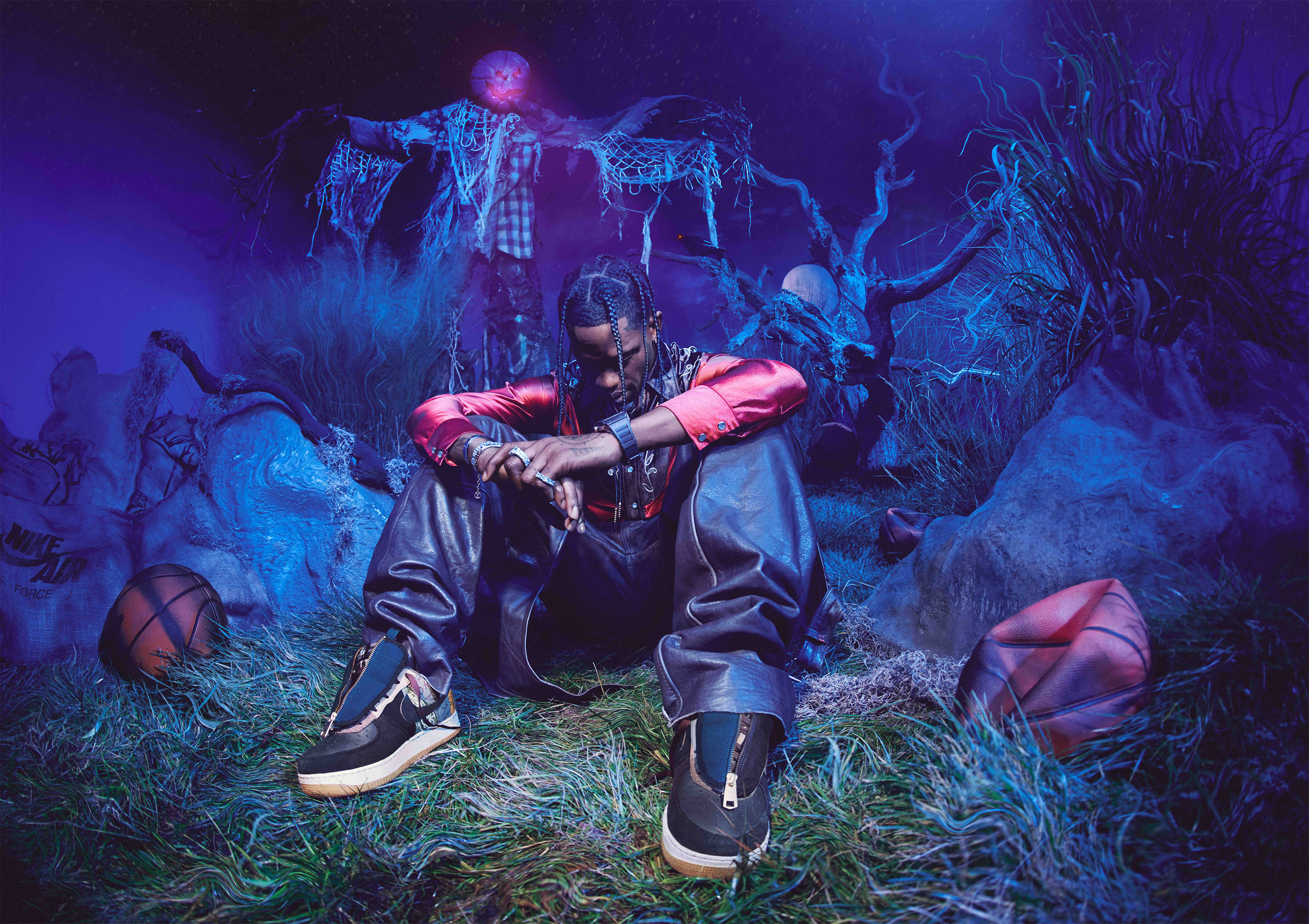 Cactus Jack x Nike 壁紙 — 一個身穿紅黑衣服的男人坐在草地上，周圍環繞著詭異發光的人物和籃球，在紫色燈光下。