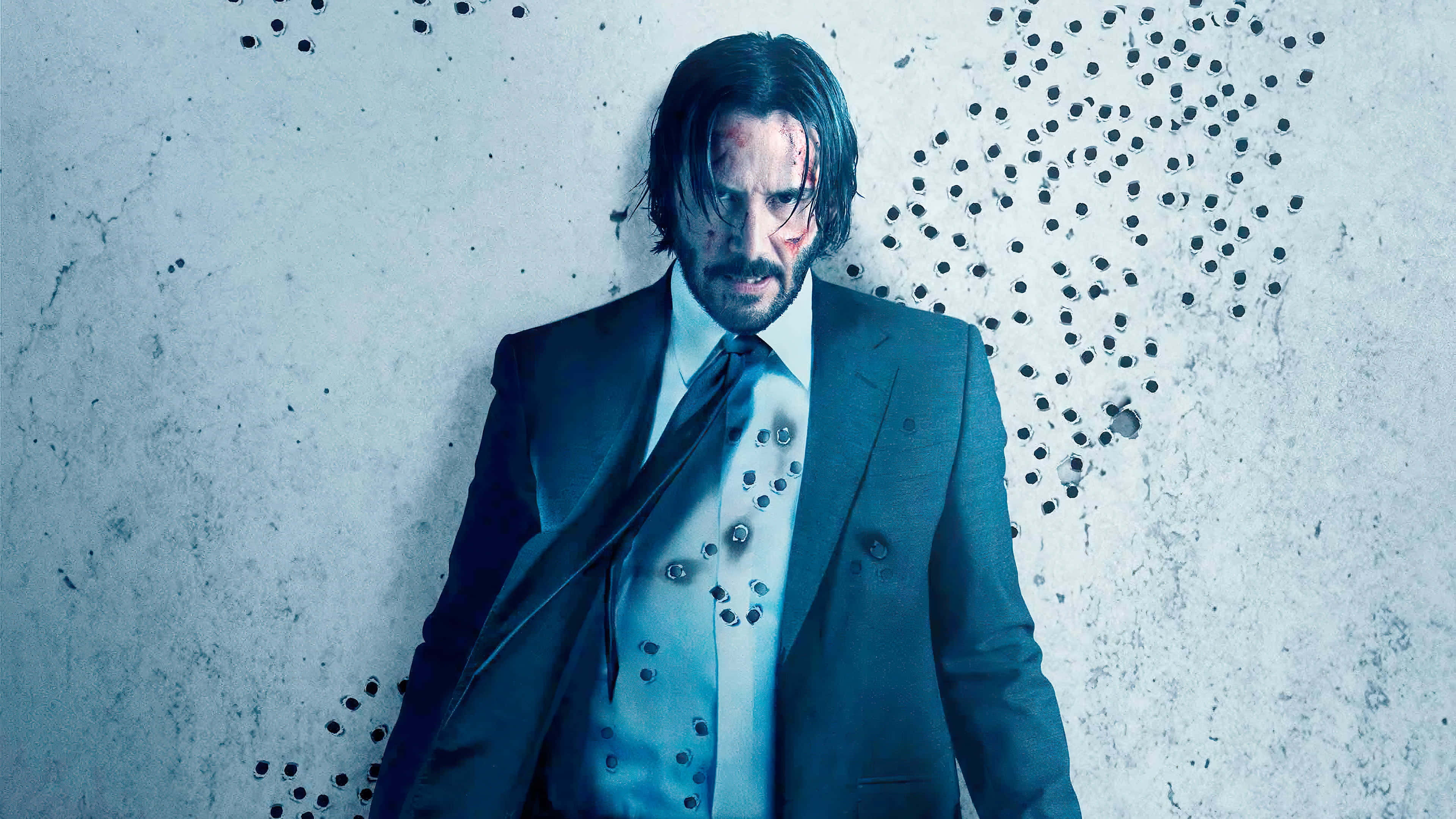 Keanu Reeves 桌布 壁紙 — 一個身穿血跡斑斑西裝的男人，表情陰沉地靠在一面佈滿彈孔的牆上。