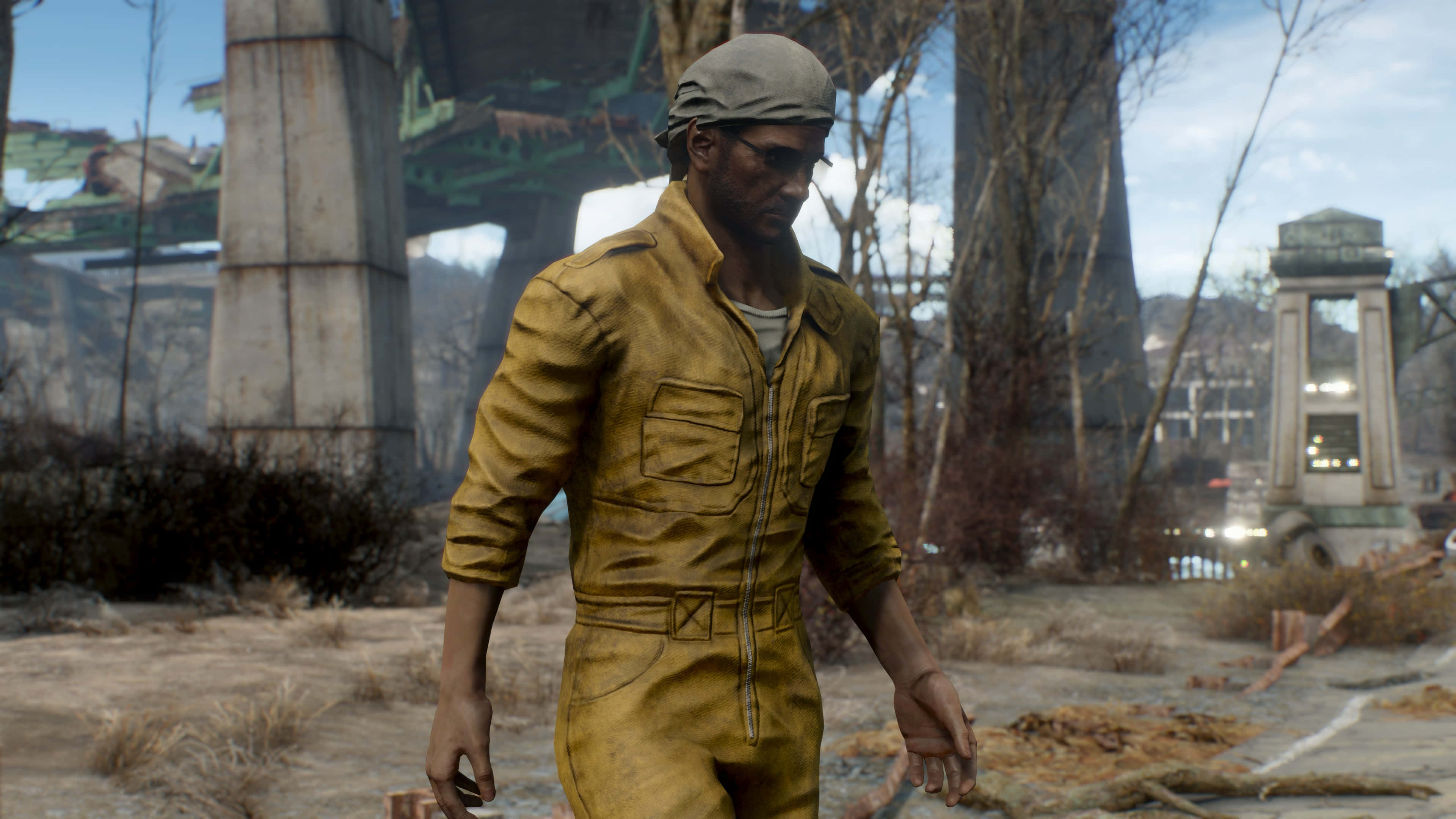 Fallout 4 The Capital Wasteland 桌布 壁紙 — 一個身穿黃色連身工作服的強壯男子，走過一片荒涼、後末日風格的廢墟，到處是破碎的混凝土和光禿的樹木。