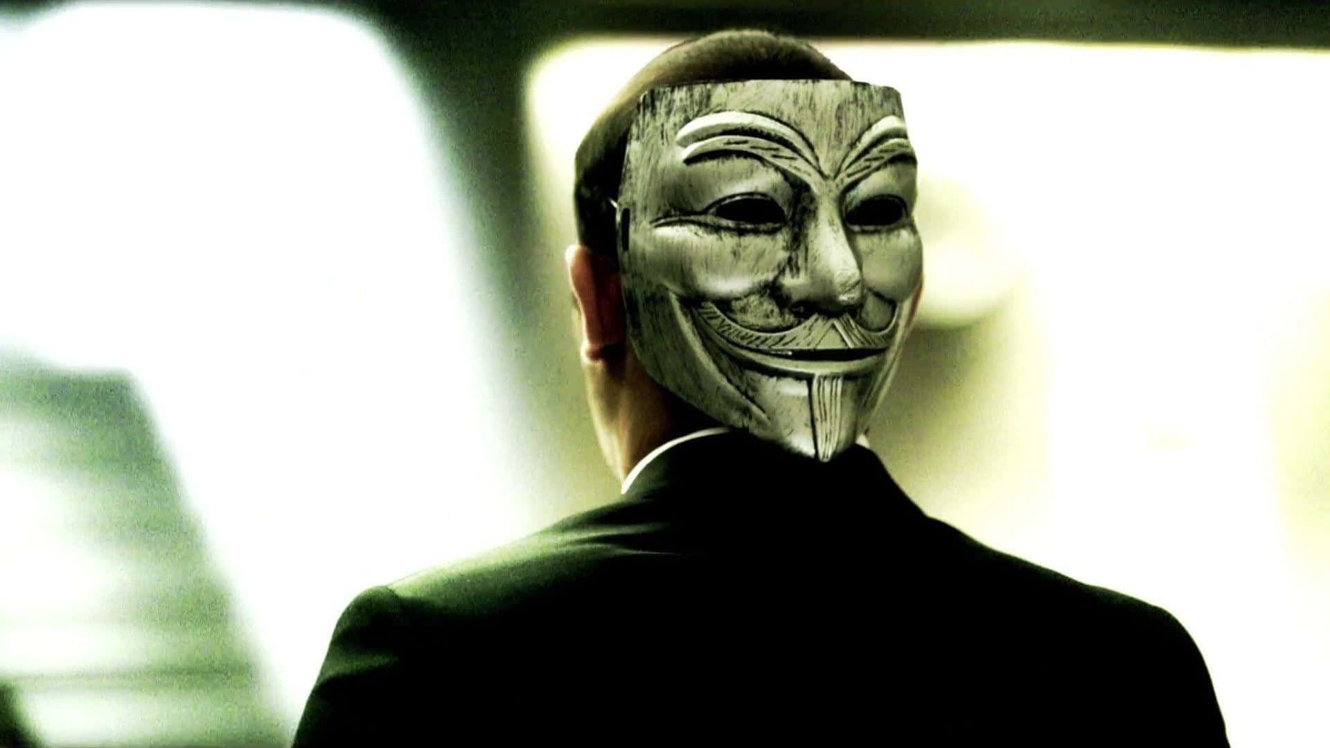 Anonymous 桌布 壁紙 — 一個身穿黑色西裝的人戴着蓋伊·福克斯面具，背對鏡頭站在光線昏暗的空間中。