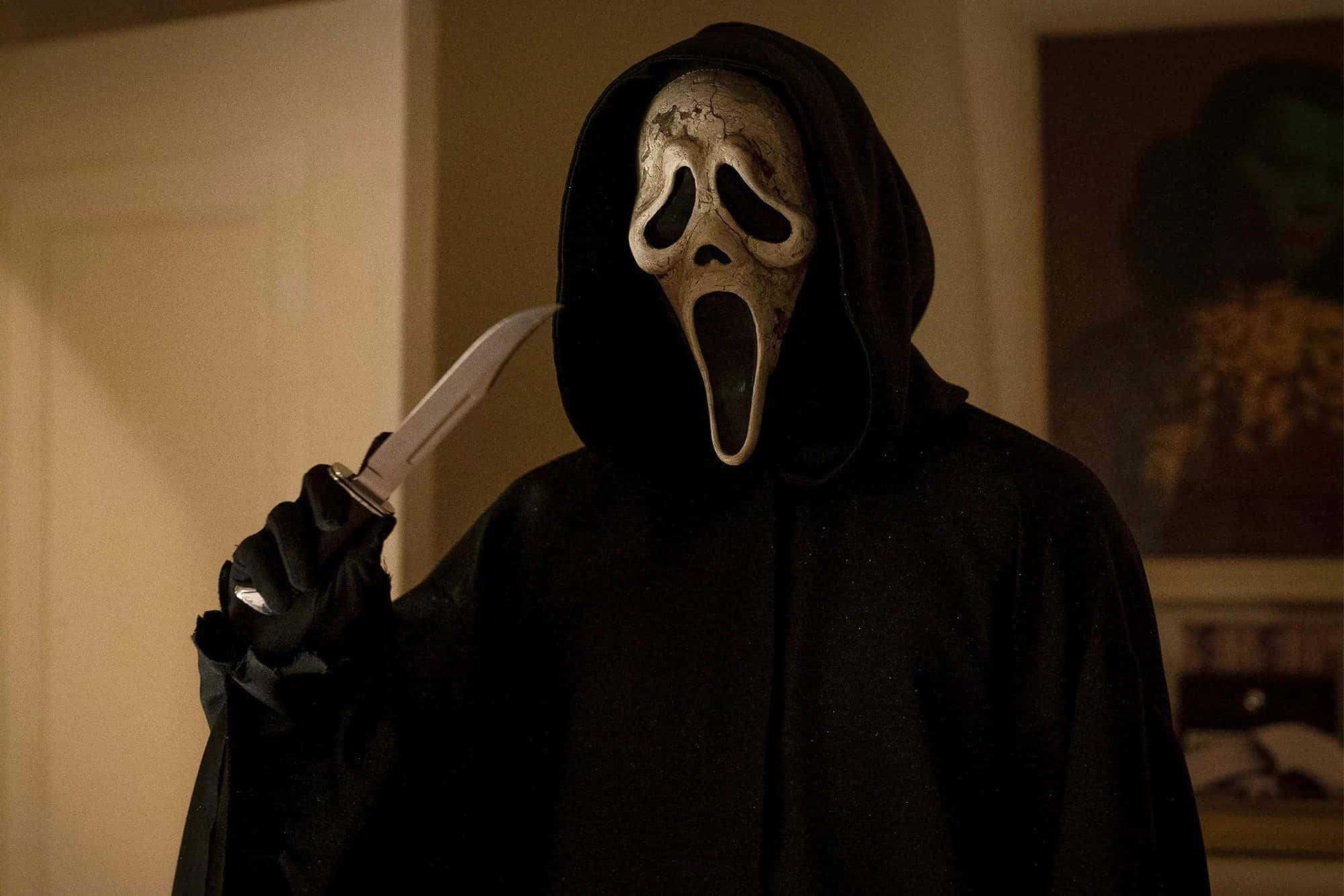 Halloween Masks 桌布 壁紙 — 一個身穿黑色連帽長袍、戴著標誌性白色驚聲尖叫面具的人物，在昏暗的室內環境中手持一把刀。