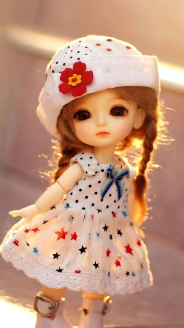 Doll 桌布 壁紙 — 一個辮子頭髮的洋娃娃，戴著白色圓點帽子，上面有一朵紅花，穿著相配的星星圖案連衣裙，沐浴在溫暖的金色陽光下。