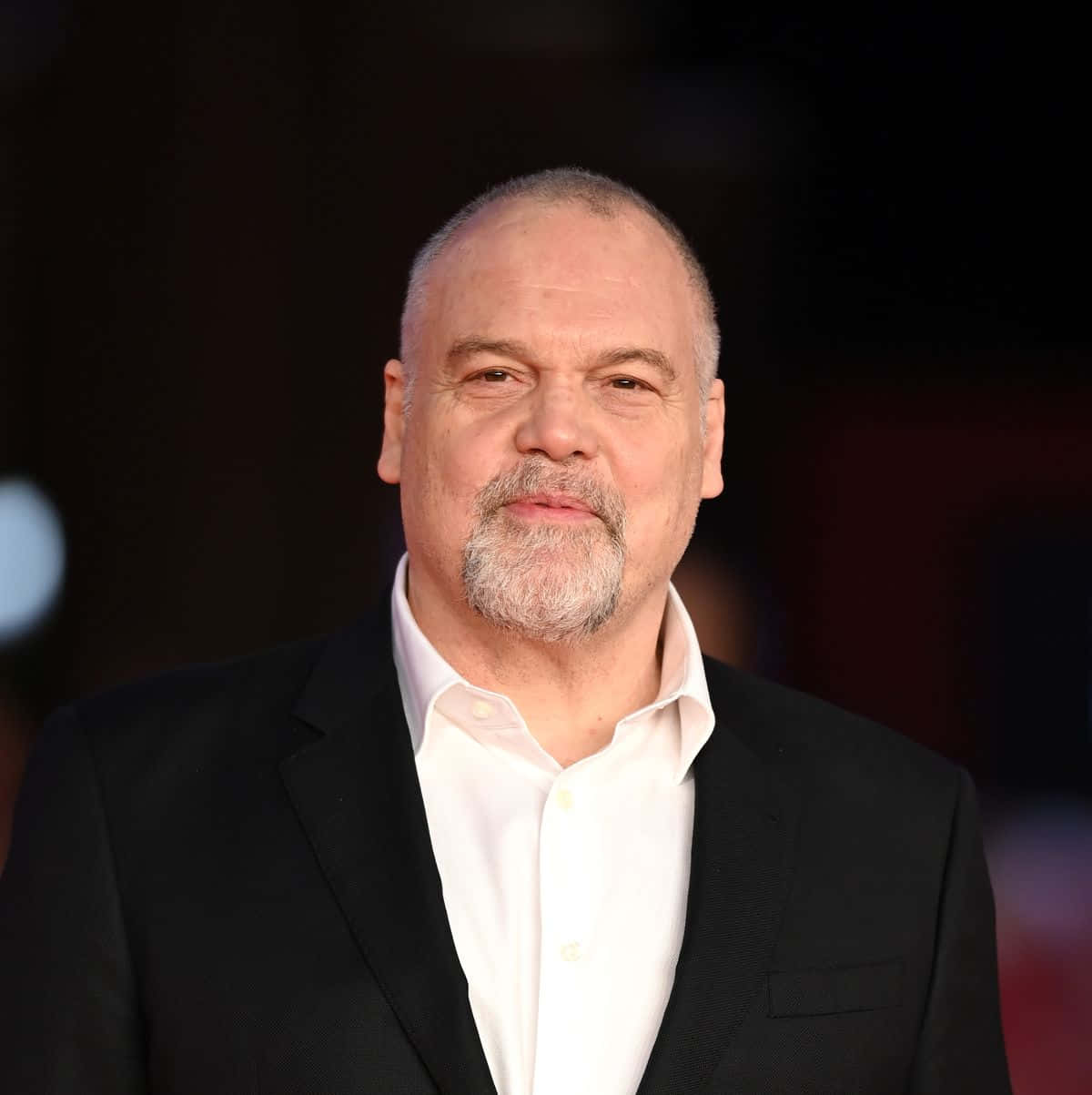 Vincent D'onofrio 桌布 壁紙 — 一個近距離肖像，一位禿頭、灰色鬍鬚的男子，身穿黑色西裝和白色襯衫，背景是黑暗模糊的。
