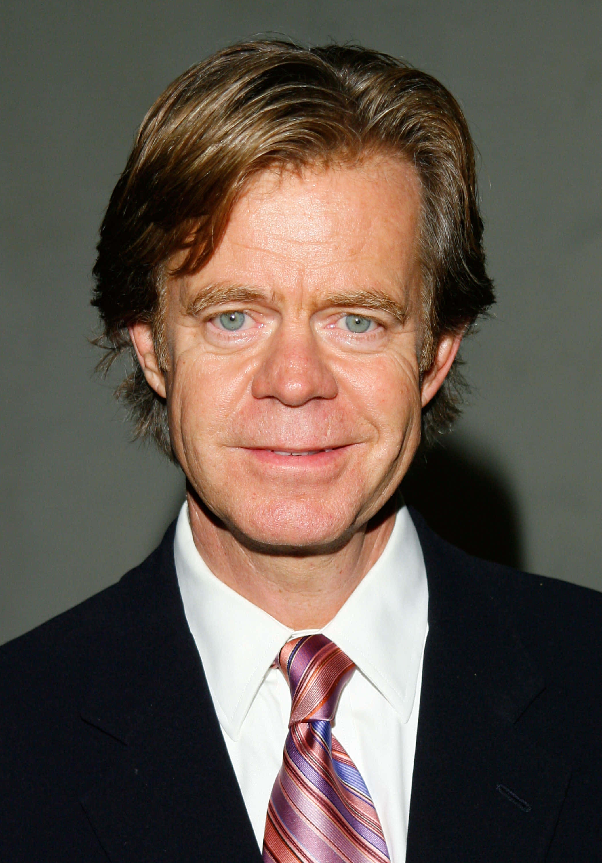 william h. macy 桌布 壁紙 — 一個近距離肖像，一名擁有淺藍色眼睛和棕色頭髮的男子，身穿深色西裝和條紋領帶，背景為灰色。