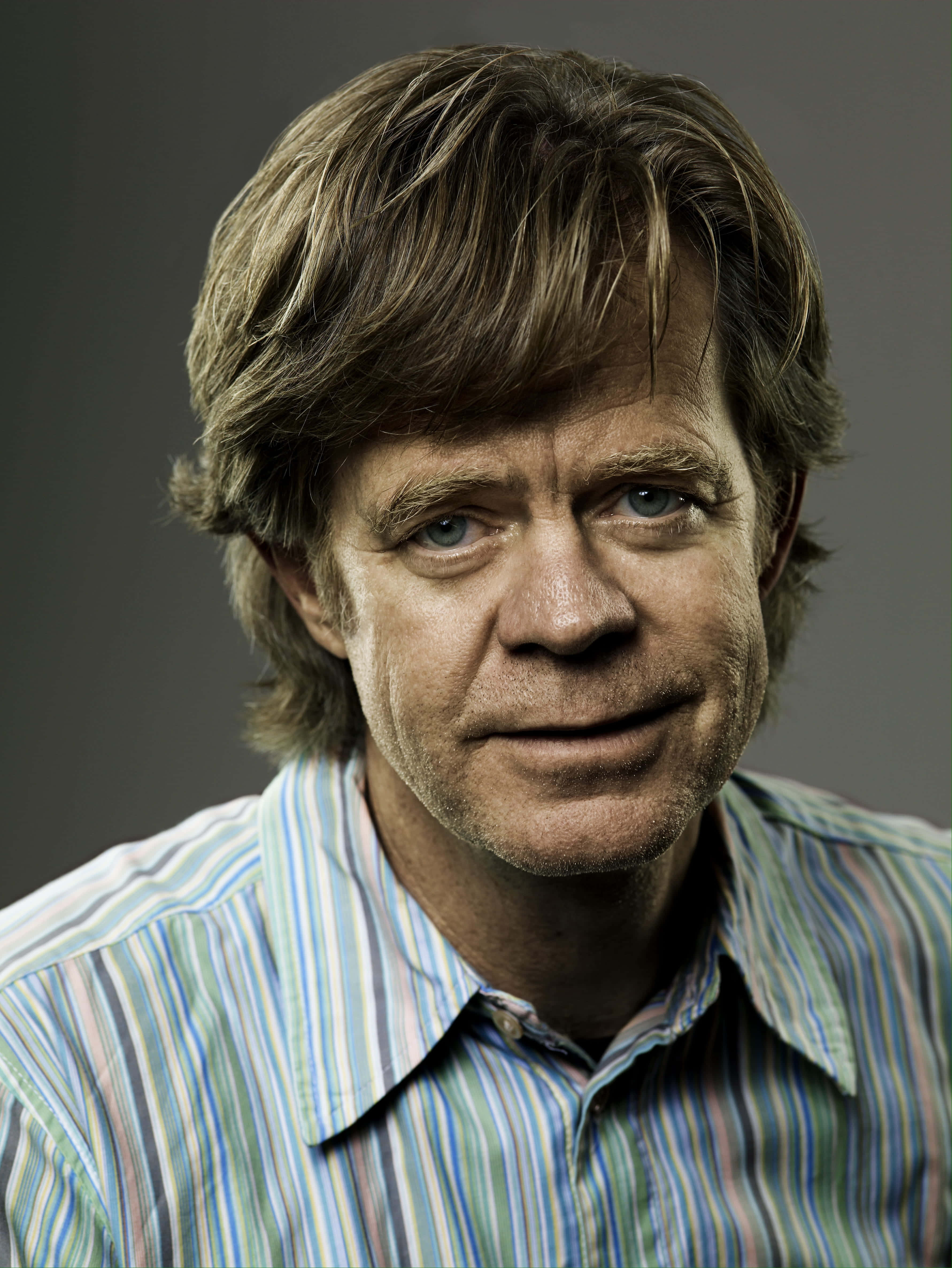 william h. macy 桌布 壁紙 — 一個近距離肖像，一名男子擁有凌亂的棕色頭髮和藍色眼睛，穿著條紋襯衫，背景為灰色。