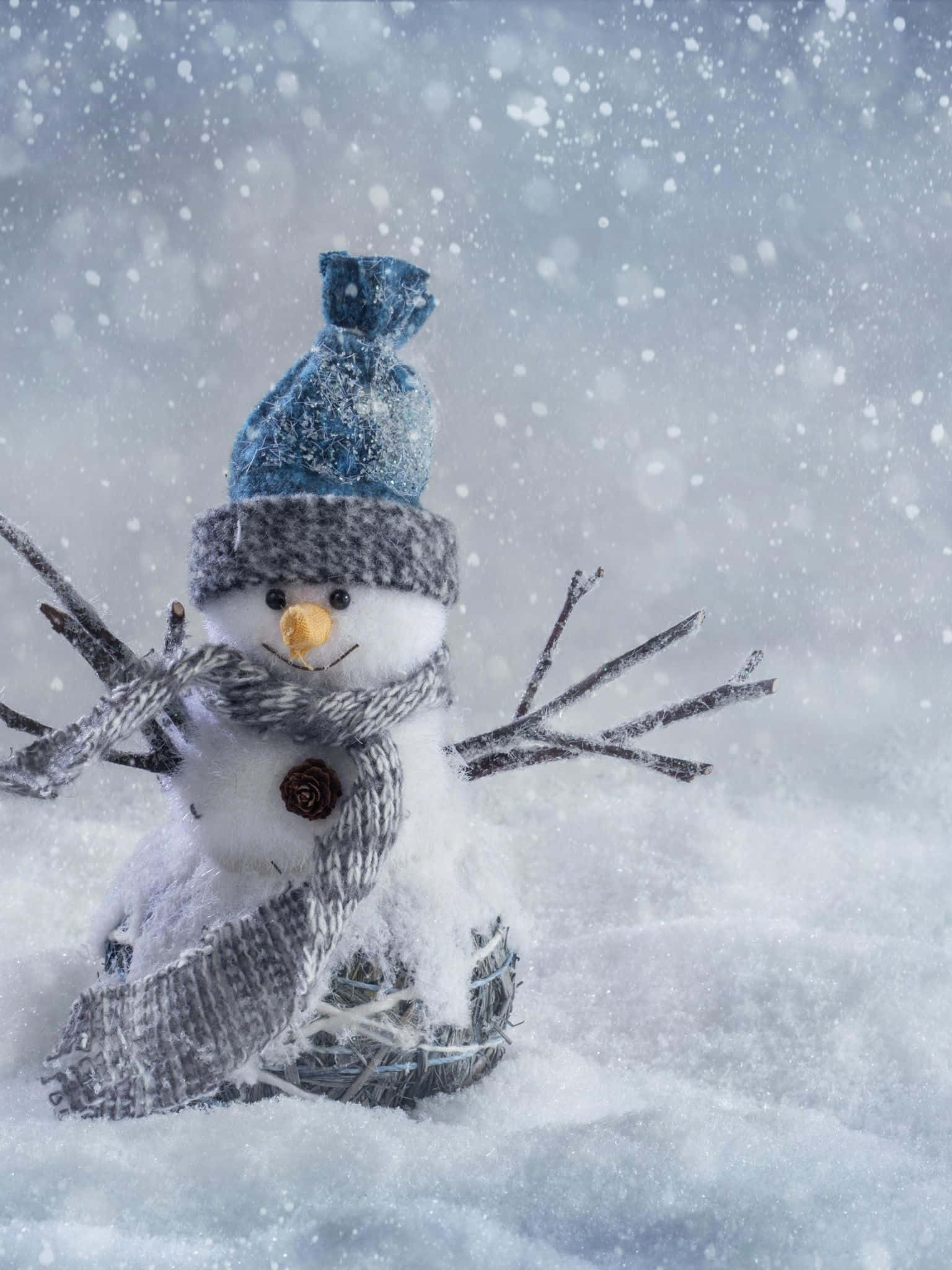 Winter Phone 桌布 壁紙 — 一個迷人的雪人，戴著藍色針織帽和灰色圍巾，站在雪景中，雪花輕輕飄落在周圍。