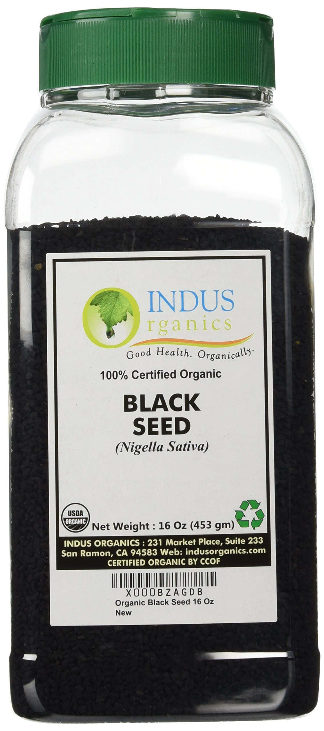 Black Cumin 桌布 壁紙 — 一個透明塑膠罐裝滿黑色種子，標有「INDUS ORGANICS Black Seed」，帶綠色蓋子。