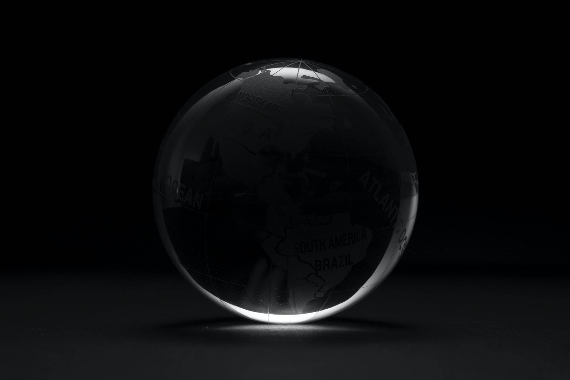 globe 桌布 壁紙 — 一個透明玻璃地球儀，上面蝕刻著大陸，在黑色背景上柔和地發光。