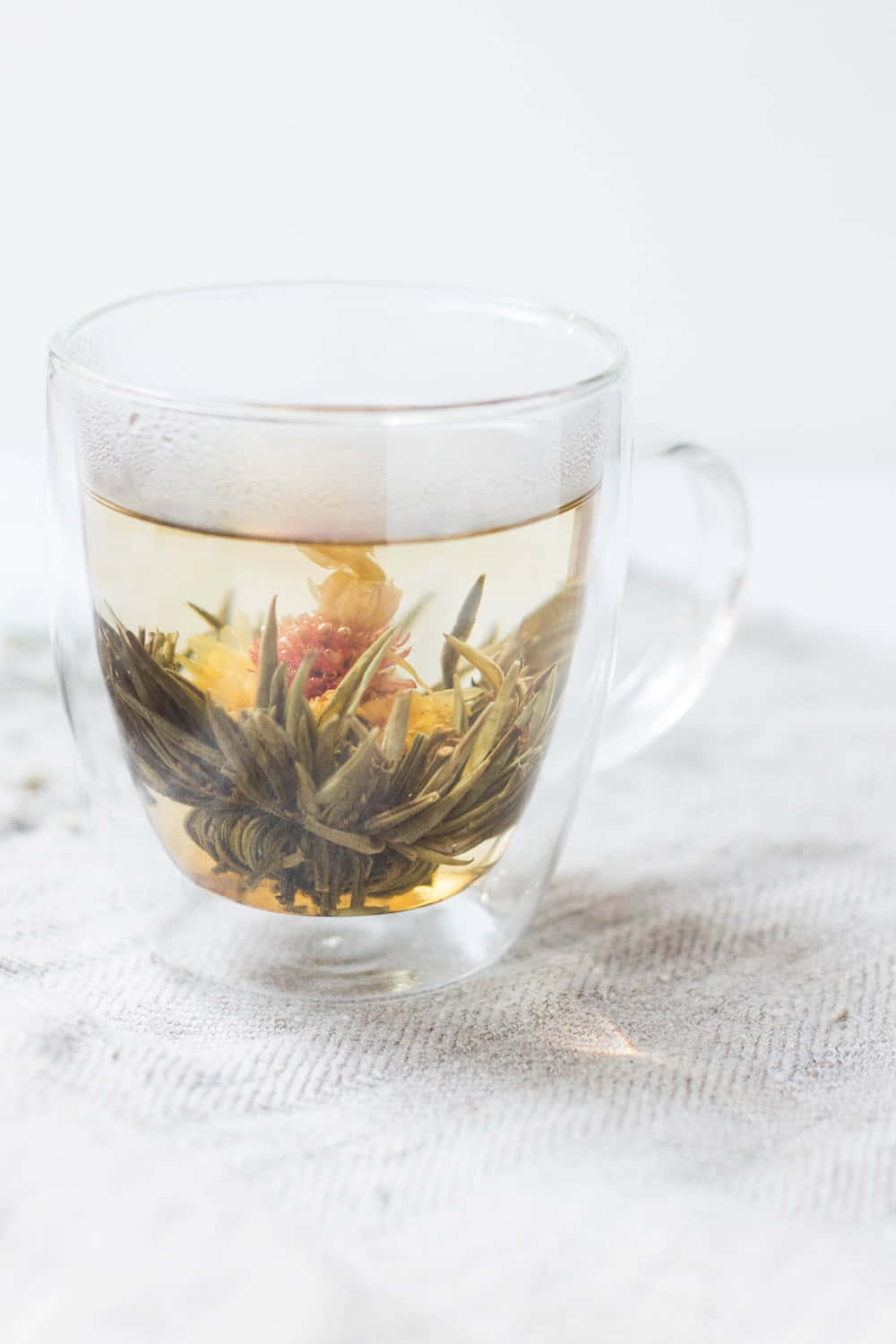 Floral Tea 桌布 壁紙 — 一個透明玻璃杯盛載著盛開的花草茶，可見綠色葉片和紅色莓果在金黃色液體中浸泡。