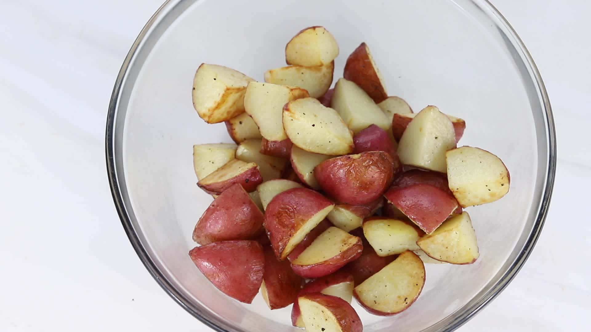 Red Potatoes 桌布 壁紙 — 一個透明玻璃碗盛載著烤紅薯，邊緣呈金黃色，可見調味料，背景為白色大理石。