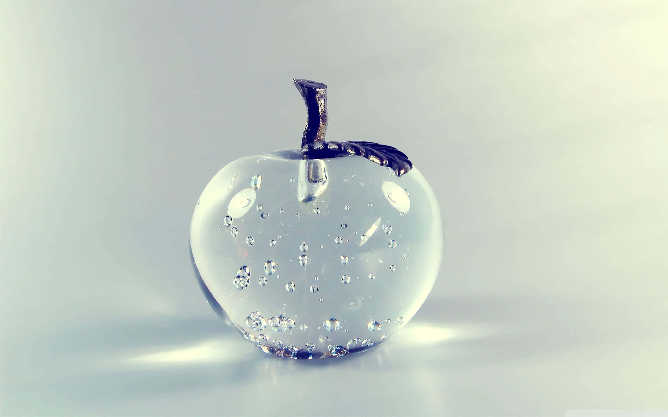 Crystal Ball 桌布 壁紙 — 一個透明玻璃蘋果雕塑，帶有氣泡和深色莖，放置在柔和的漸變背景上。