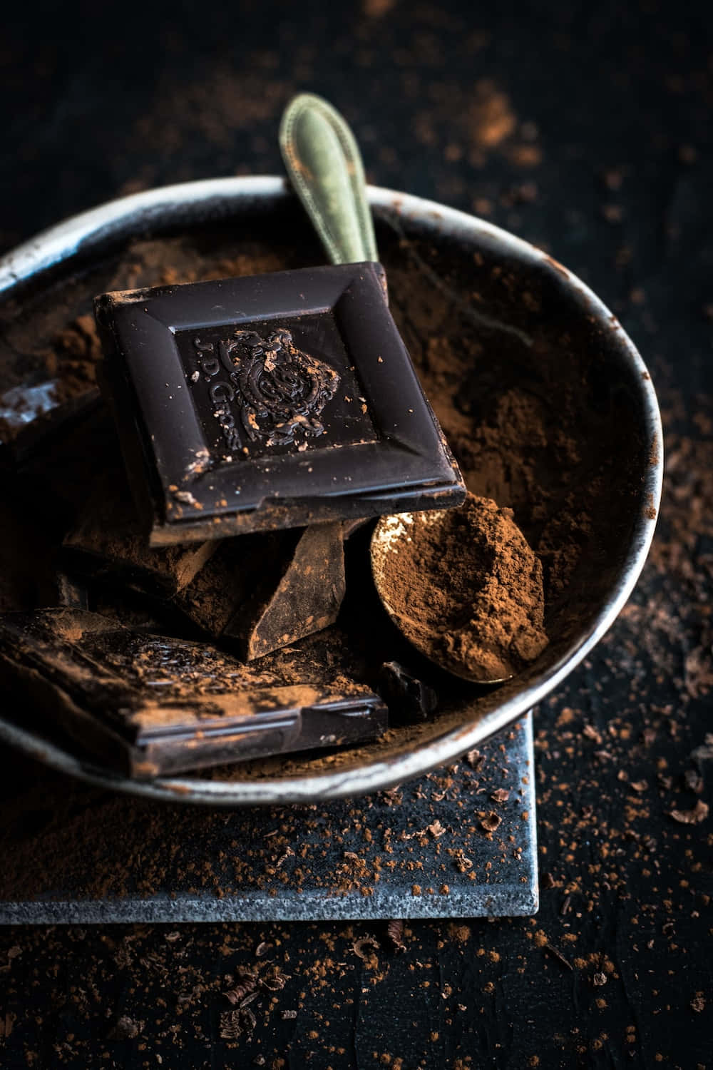 Dark Chocolate 桌布 壁紙 — 一個鄉村風格的碗裡盛著濃郁的黑朱古力條和可可粉，配上一把復古勺子，背景是深色紋理。