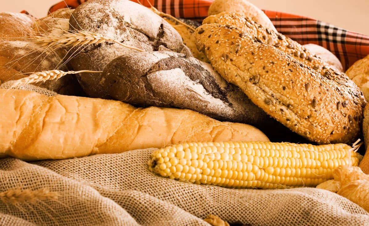 Corn 桌布 壁紙 — 一個鄉村風格的籃子裡裝著金黃色的粟米和各種撒上麵粉和種子的手工麵包。