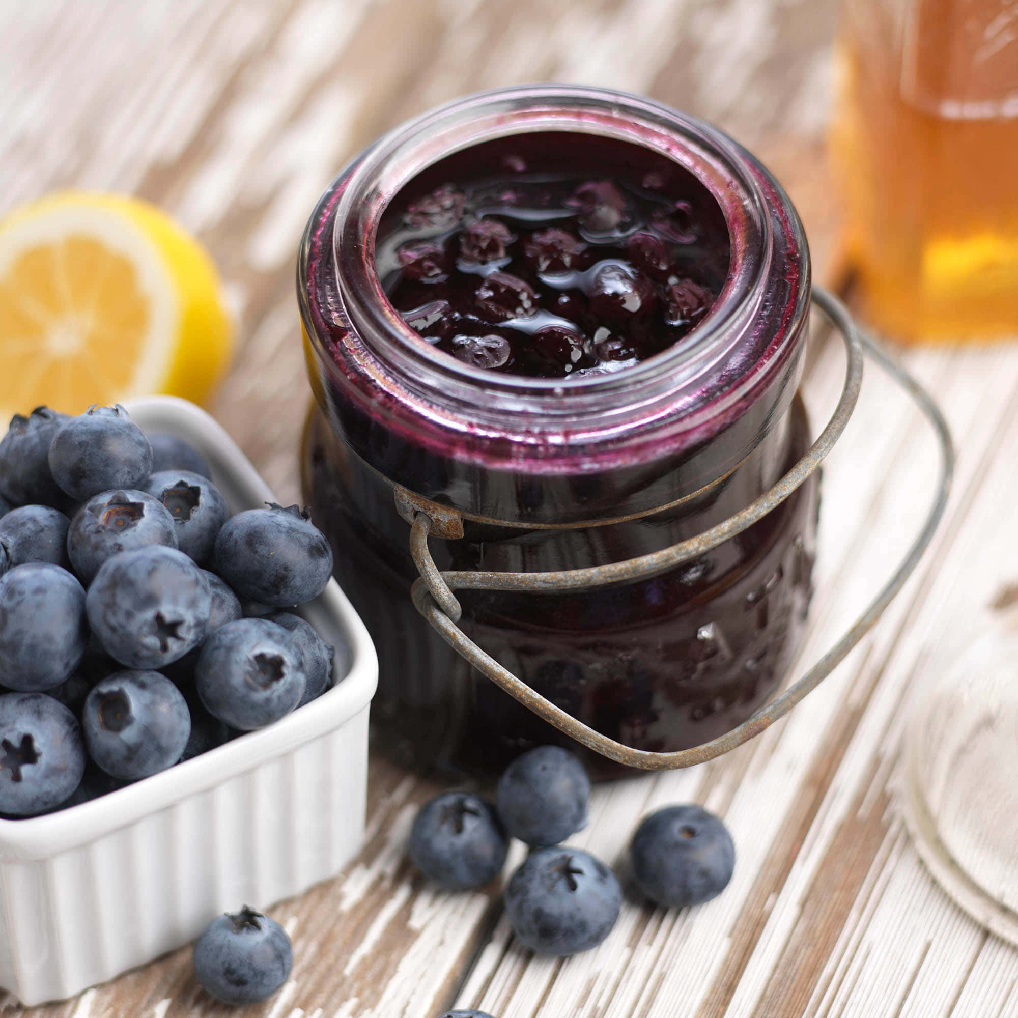 Blueberry Jam 桌布 壁紙 — 一個鄉村風格的自家製藍莓醬罐子，旁邊放著新鮮莓果、檸檬和蜂蜜，置於一張風化的木桌上。