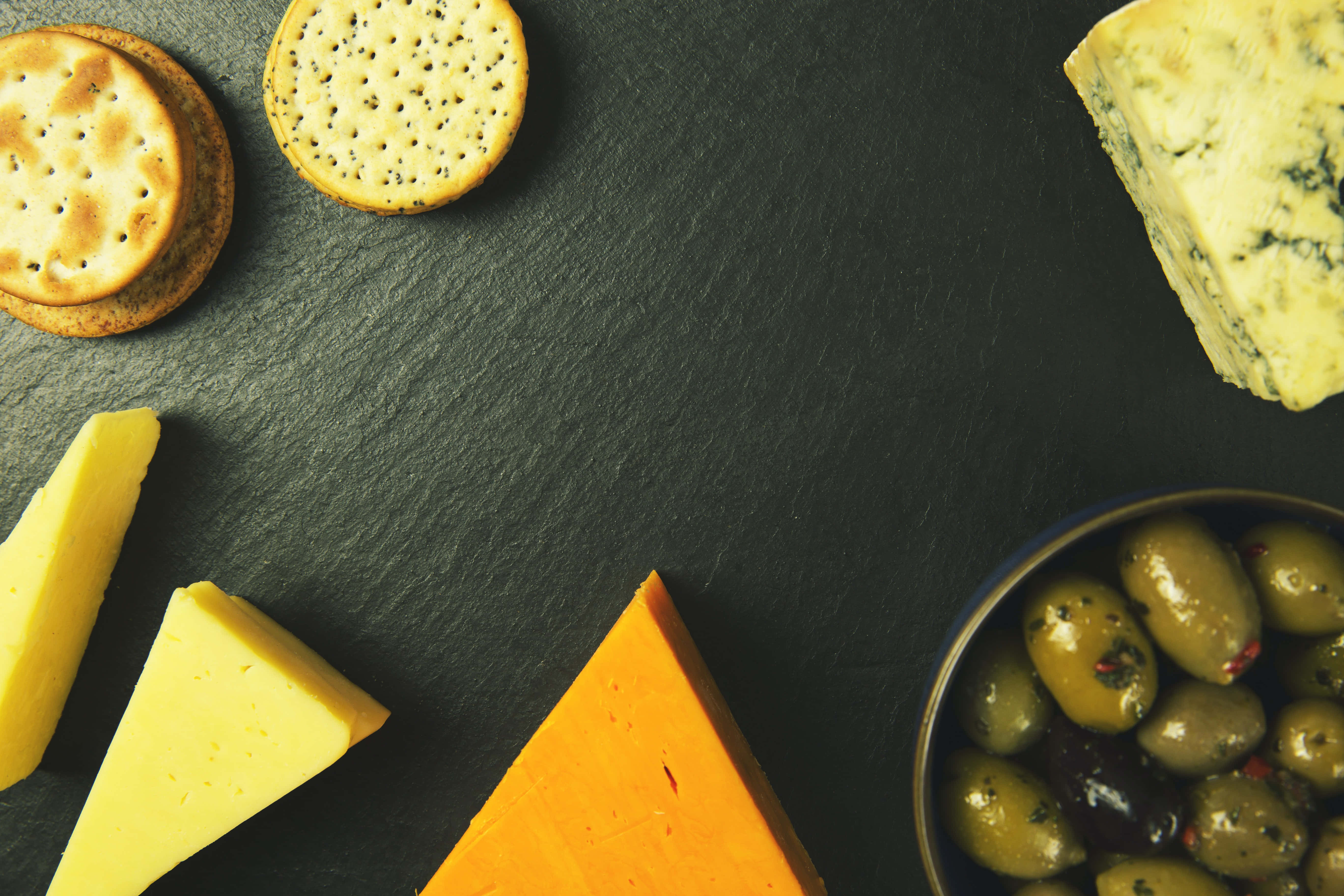 Cheese 桌布 壁紙 — 一個鄉村風格的芝士拼盤，上面擺放著各種芝士、餅乾和橄欖，置於深色石板表面上。