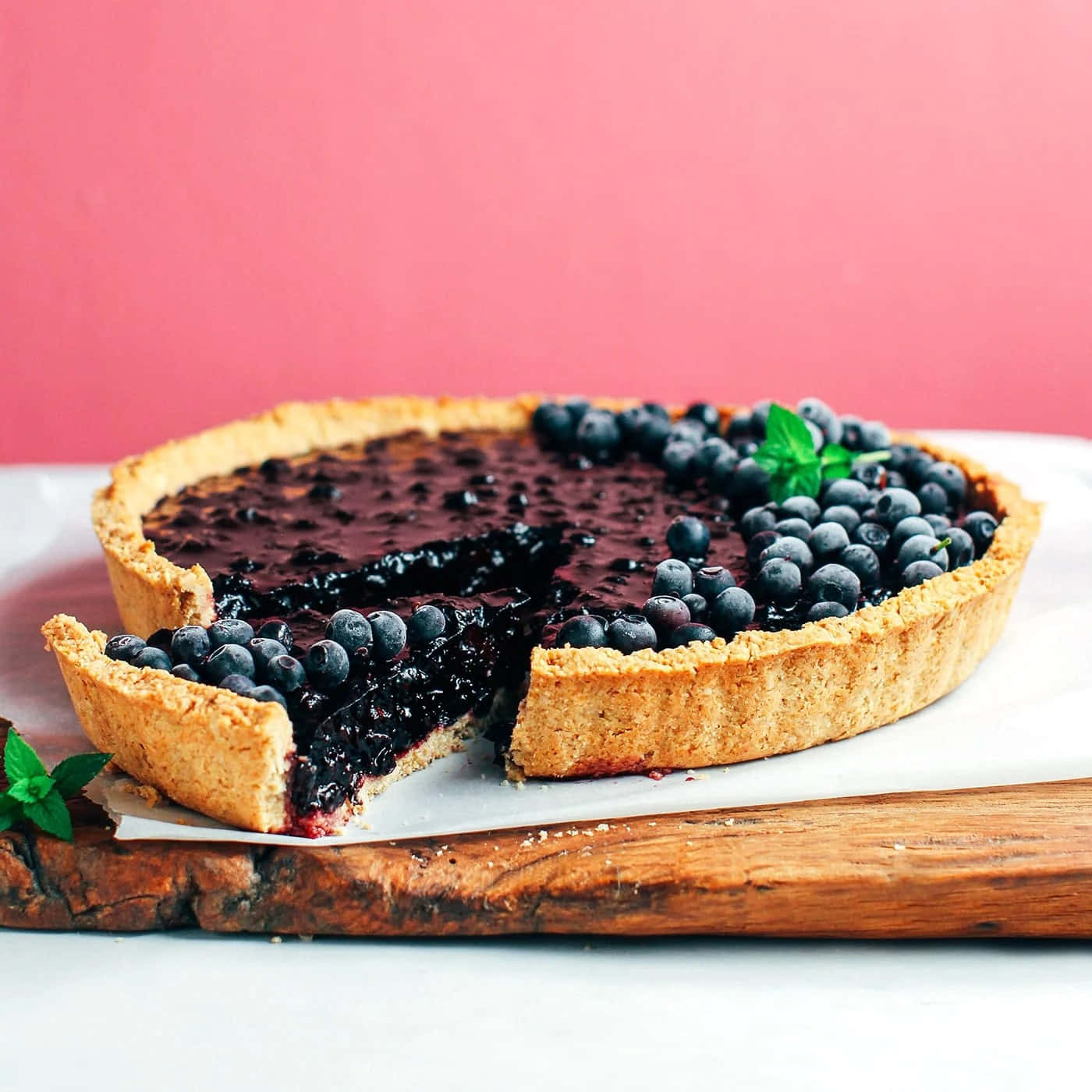 Blueberries Tart 桌布 壁紙 — 一個鄉村風格的藍莓撻，金黃色的外皮放在木板上，切開一片露出多汁的餡料和新鮮薄荷裝飾。
