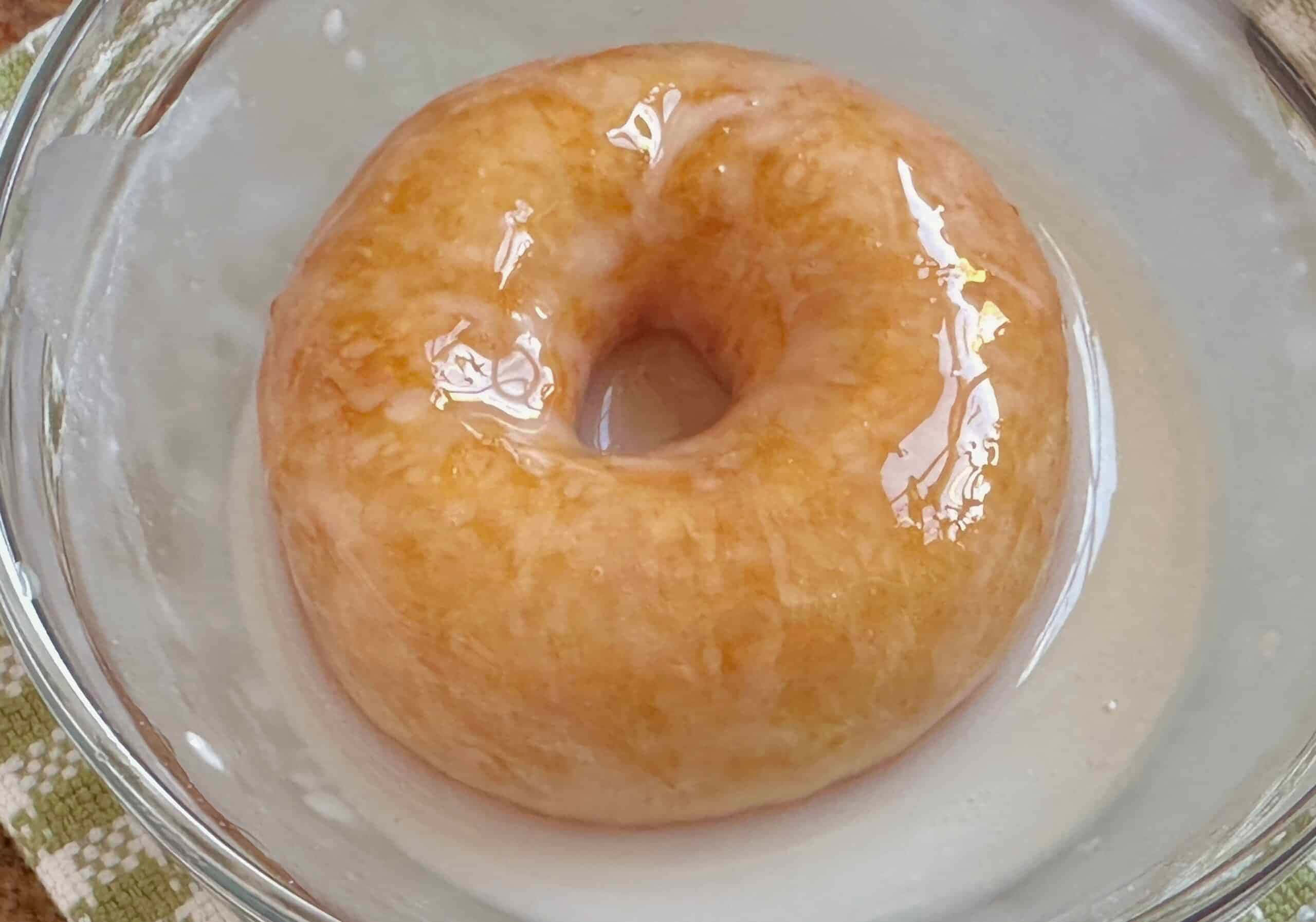 Glazed Donut 桌布 壁紙 — 一個釉面冬甩放在透明玻璃碗中，帶有光澤的糖衣反射光線。