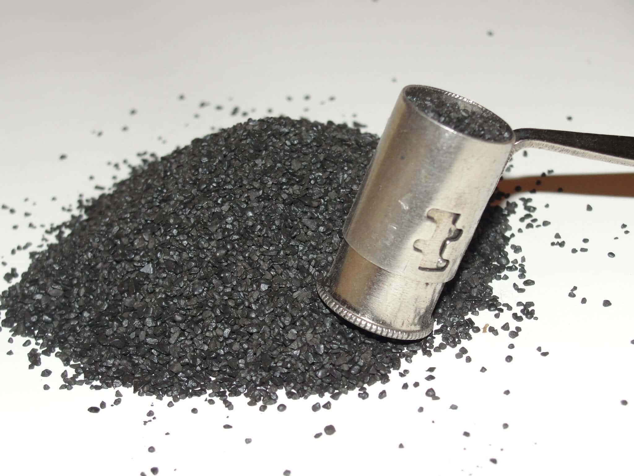 Black Powder 桌布 壁紙 — 一個金屬勺裝滿深色顆粒木炭，放在一堆上，背景是純白色。
