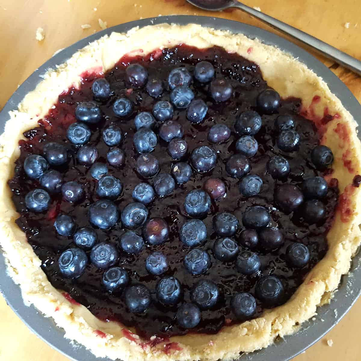 Blueberries Tart 桌布 壁紙 — 一個金屬盤中的藍莓批特寫，上面有新鮮藍莓和深色糖漿，放在木桌上。