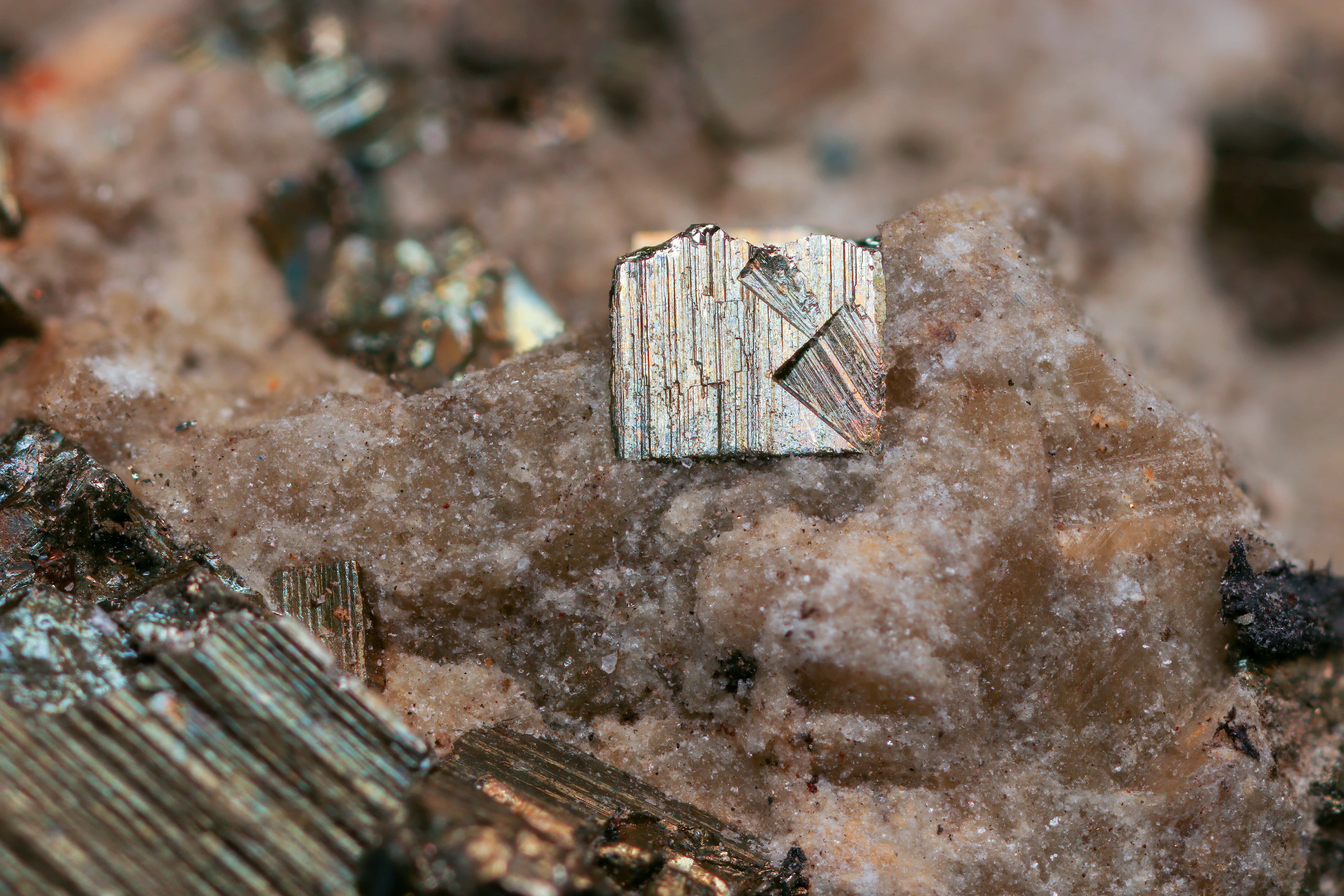 Mining 桌布 壁紙 — 一個金屬質感的黃鐵礦晶體特寫，帶有條紋晶面，放置在粗糙的褐色岩石表面上。