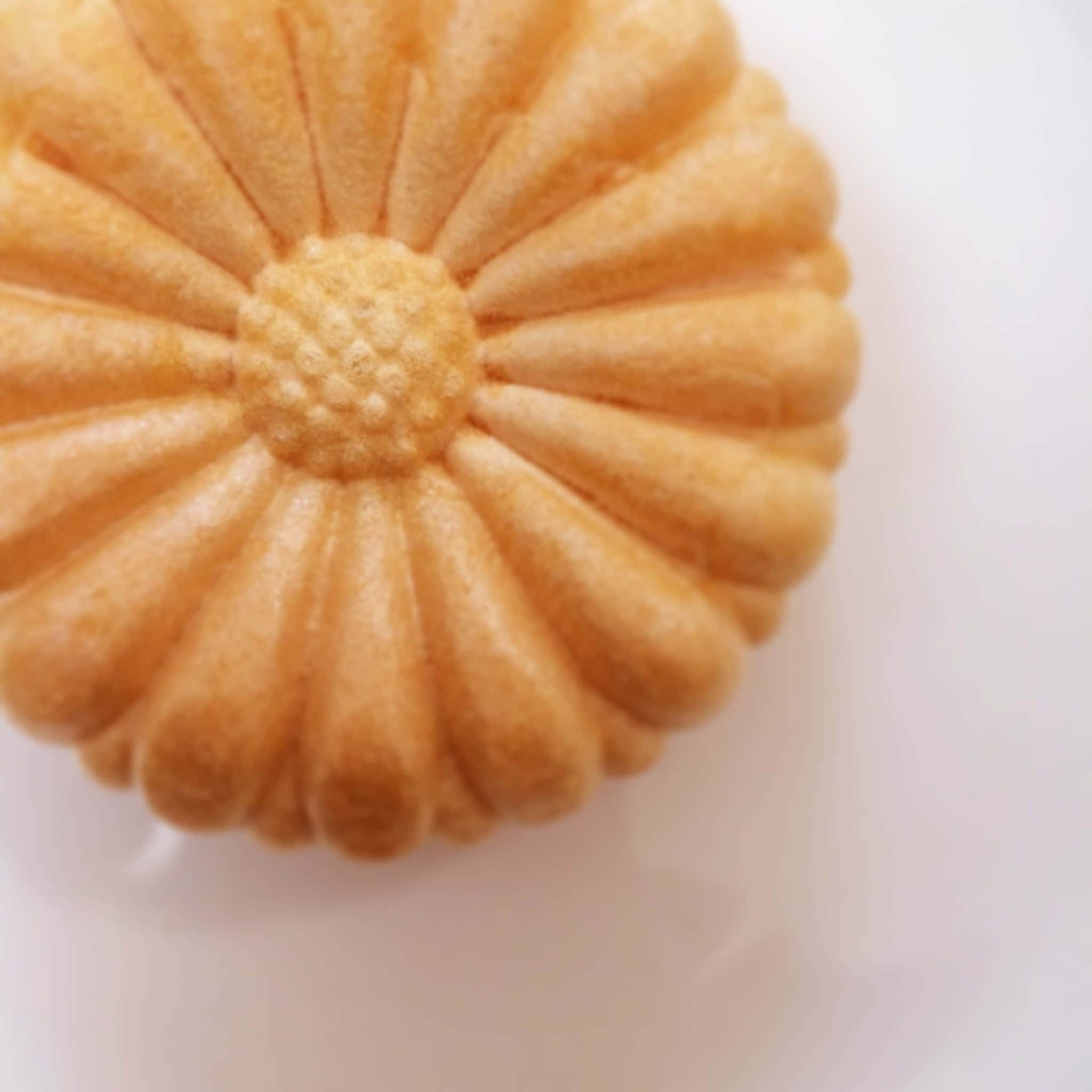 Japanese Sweets 桌布 壁紙 — 一個金棕色花形曲奇的特寫，帶有紋理花瓣，放在純白色表面上。
