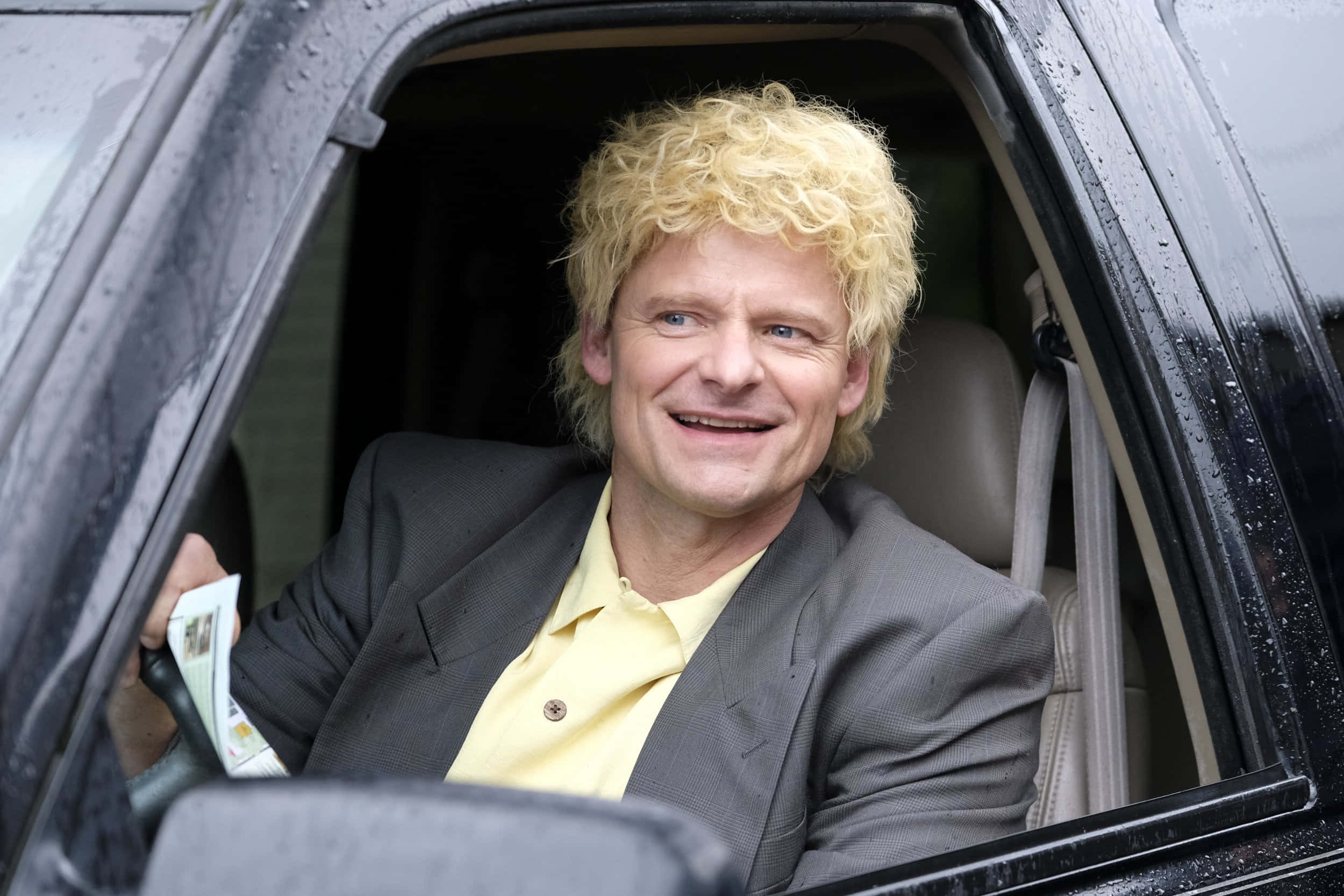 Steve Zahn 桌布 壁紙 — 一個金色捲髮的男人在雨天從車窗微笑，手持現金。