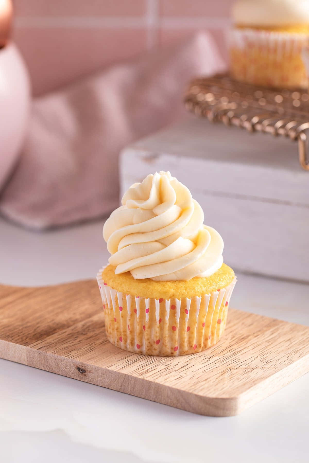 Buttercream 桌布 壁紙 — 一個金色紙杯蛋糕，上面有奶油漩渦狀糖霜，放在木板上，背景是柔和的粉紅色廚房。