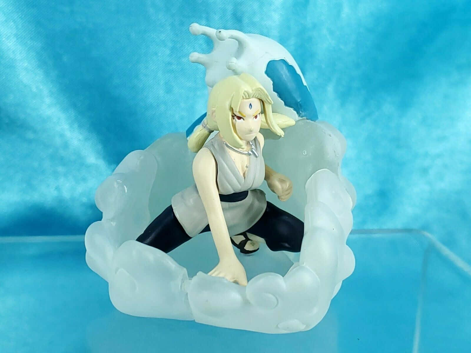 Katsuyu 桌布 壁紙 — 一個金髮角色的動漫人偶，以動態姿勢站立，周圍環繞著半透明雲朵底座，背景為帶紋理的藍色背景。