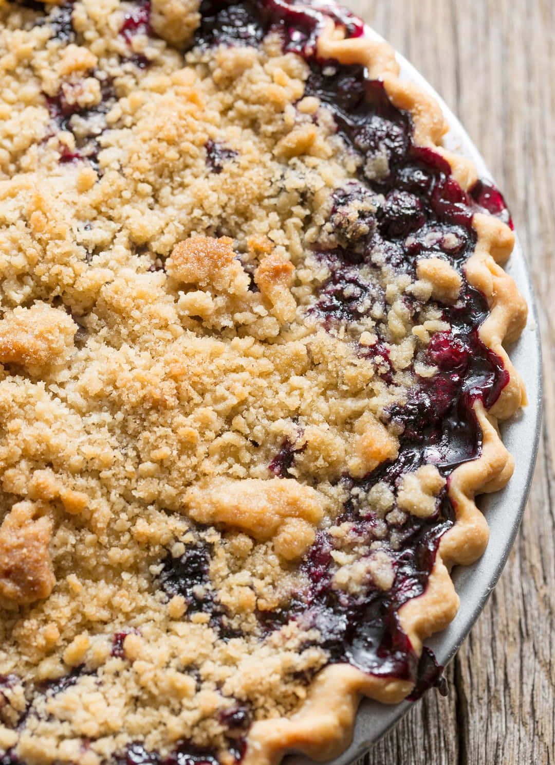 Blueberry Pie 桌布 壁紙 — 一個金黃色、鬆脆的藍莓批特寫，內有冒泡的深色水果餡料，放在質樸的木桌上。