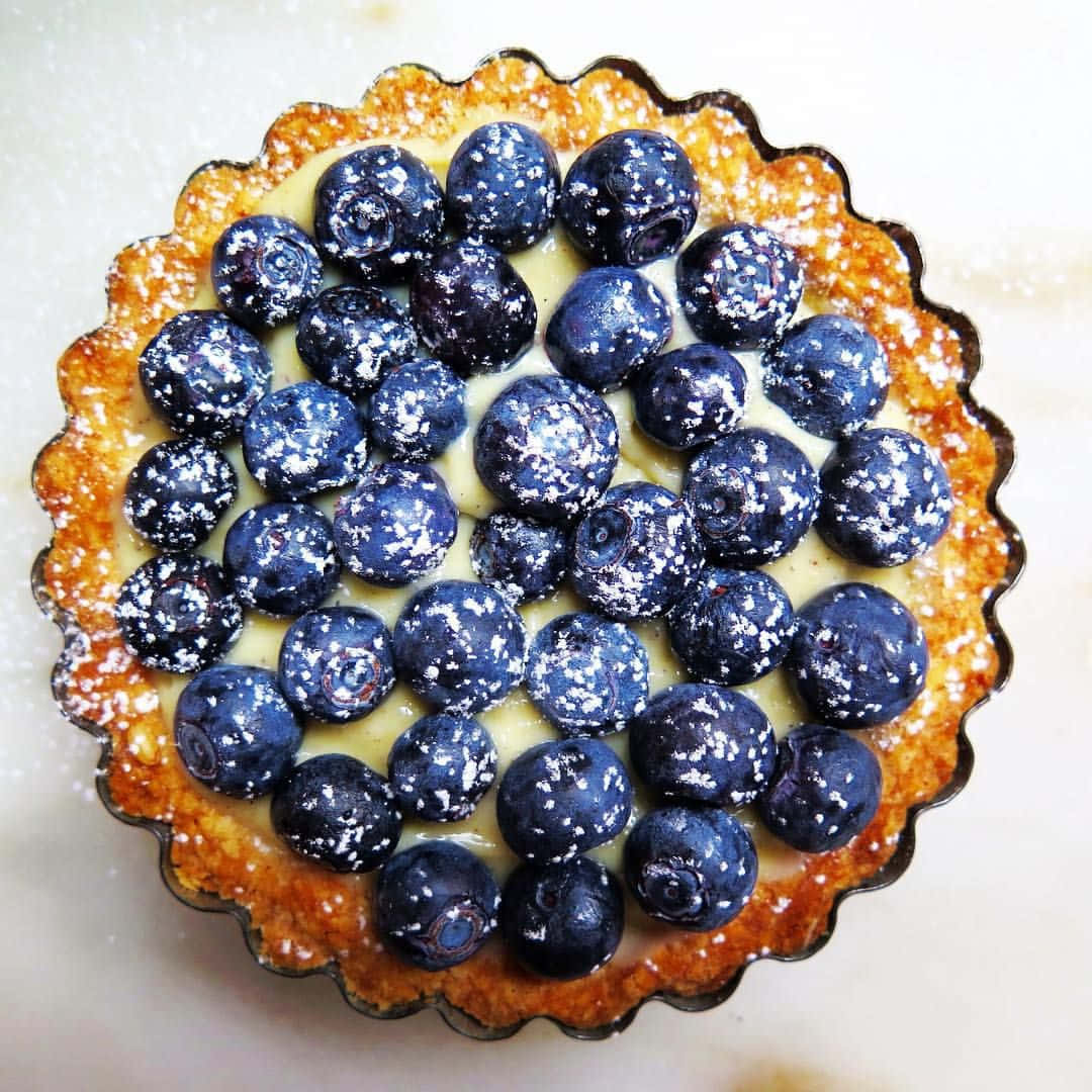 Blueberries Tart 桌布 壁紙 — 一個金黃色撻的 close-up，上面鋪滿飽滿的藍莓，撒上糖粉。