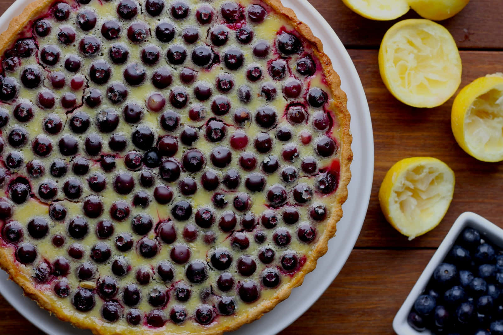 Blueberries Tart 桌布 壁紙 — 一個金黃色的藍莓撻，上面鋪滿新鮮漿果和檸檬半個，放在質樸的木桌上。